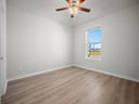 bedroom with brown flooring, a window & a ceiling fan