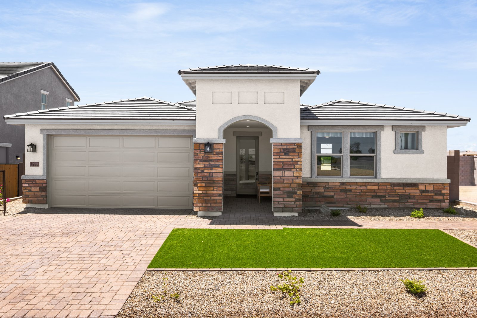 single-story home with artificial grass and paver driveway