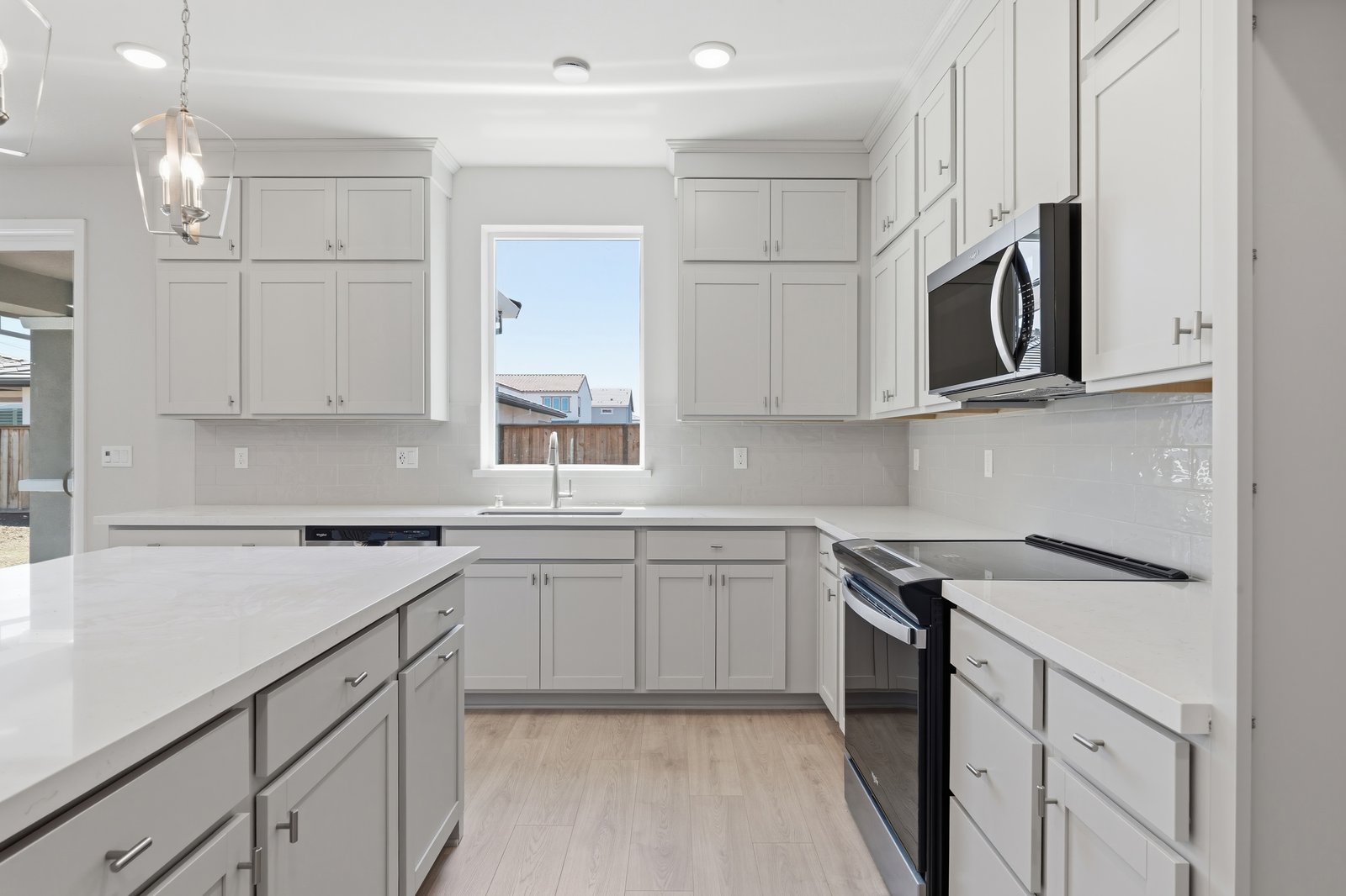 kitchen with light gray ceiling height cabinets, white counters, light wood floors, and window looking out to the backyard above sink