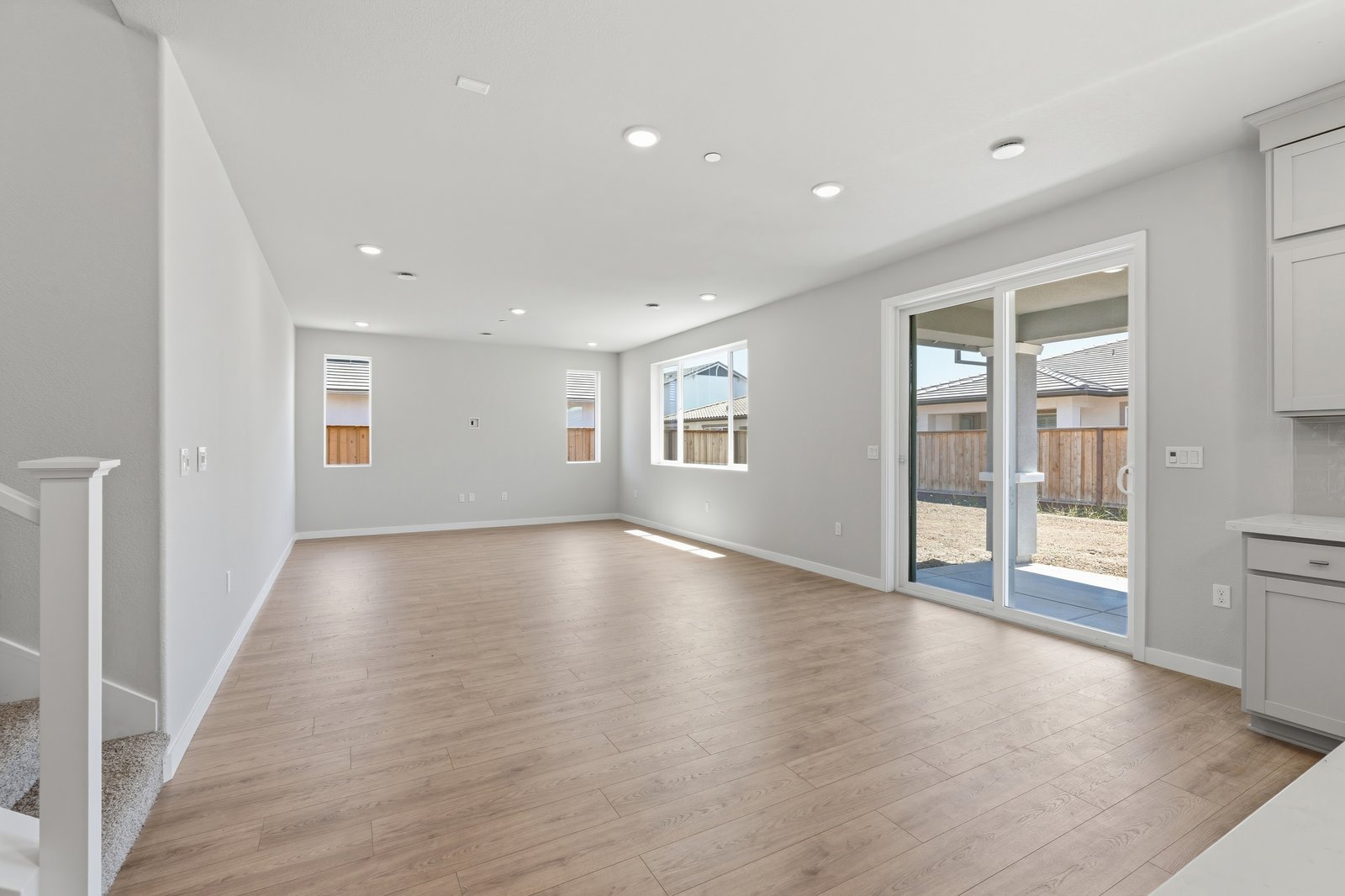 great room with light wood floors, sliding glass door to the backyard patio, multiple windows, and recessed ceiling lights