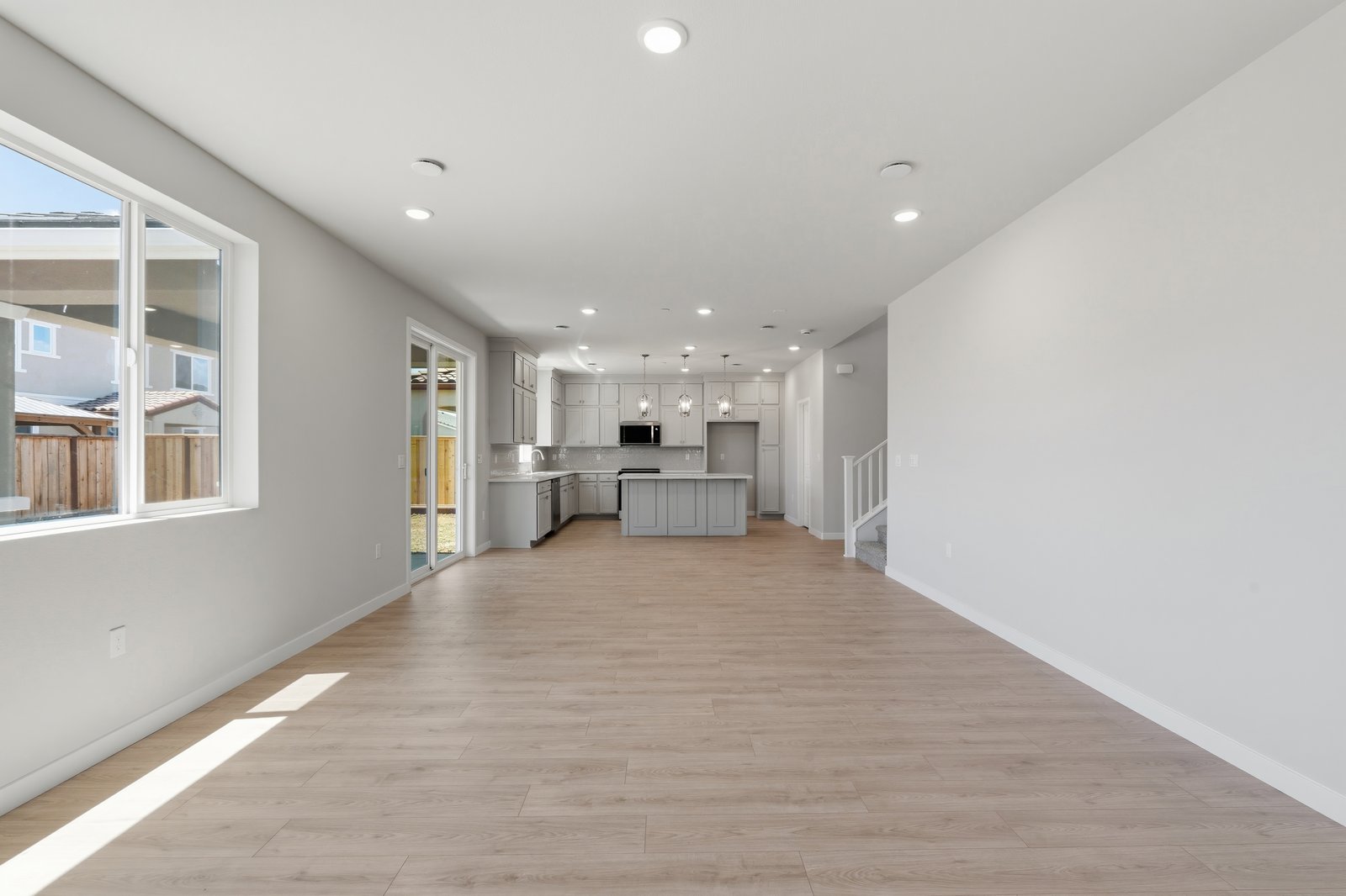 great room with light wood floors, white walls, recessed ceiling lights, window, and sliding glass door to the back covered patio
