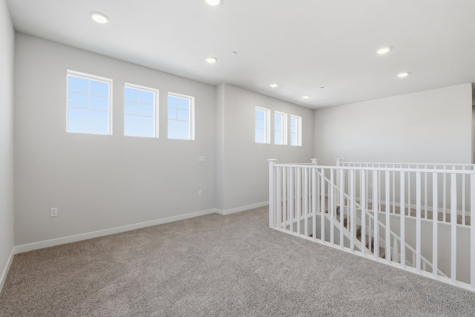 loft with tan carpet, light gray walls, and multiple windows