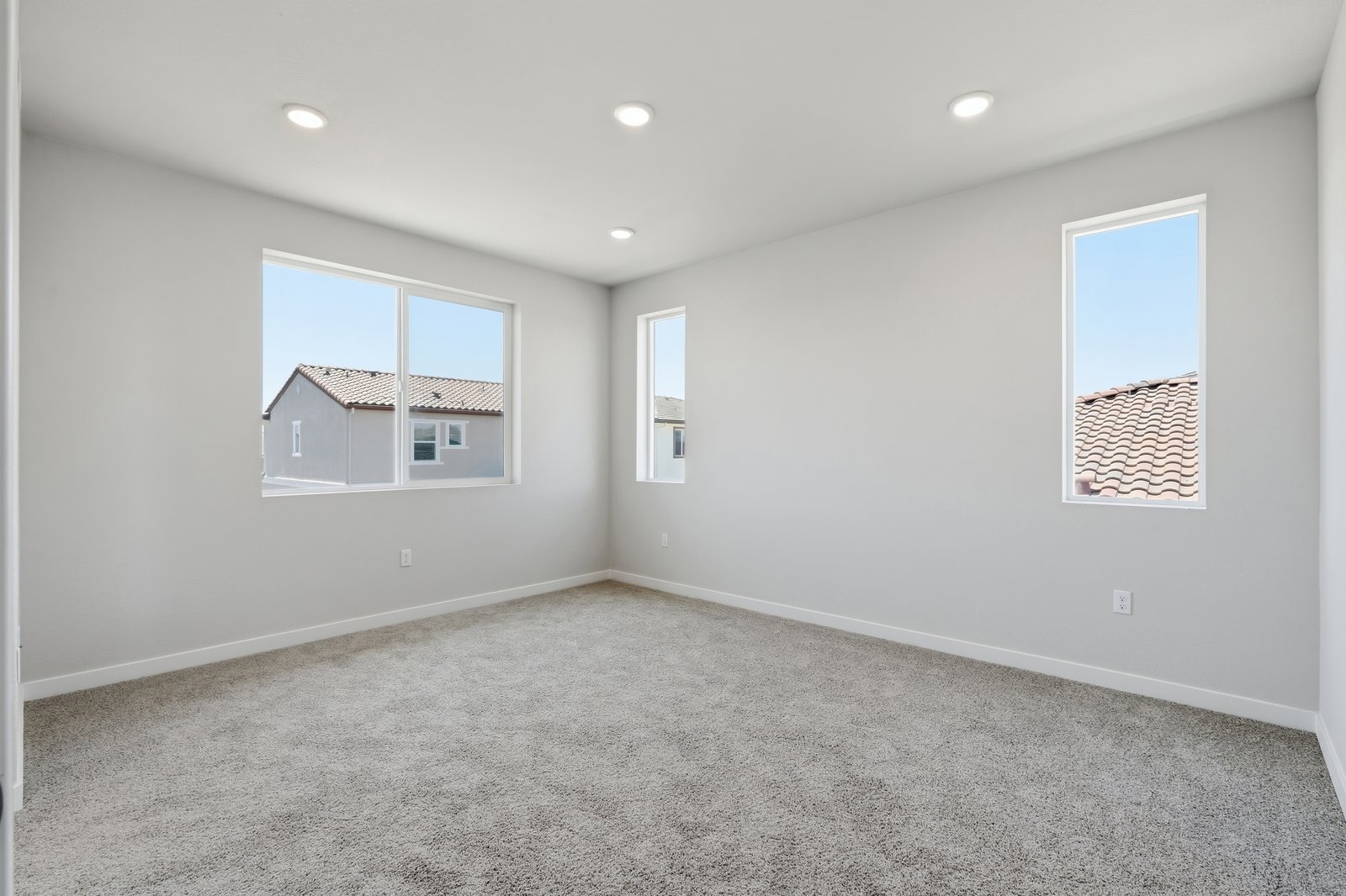 bedroom with tan carpet, light gray walls, three windows, and recessed ceiling lights