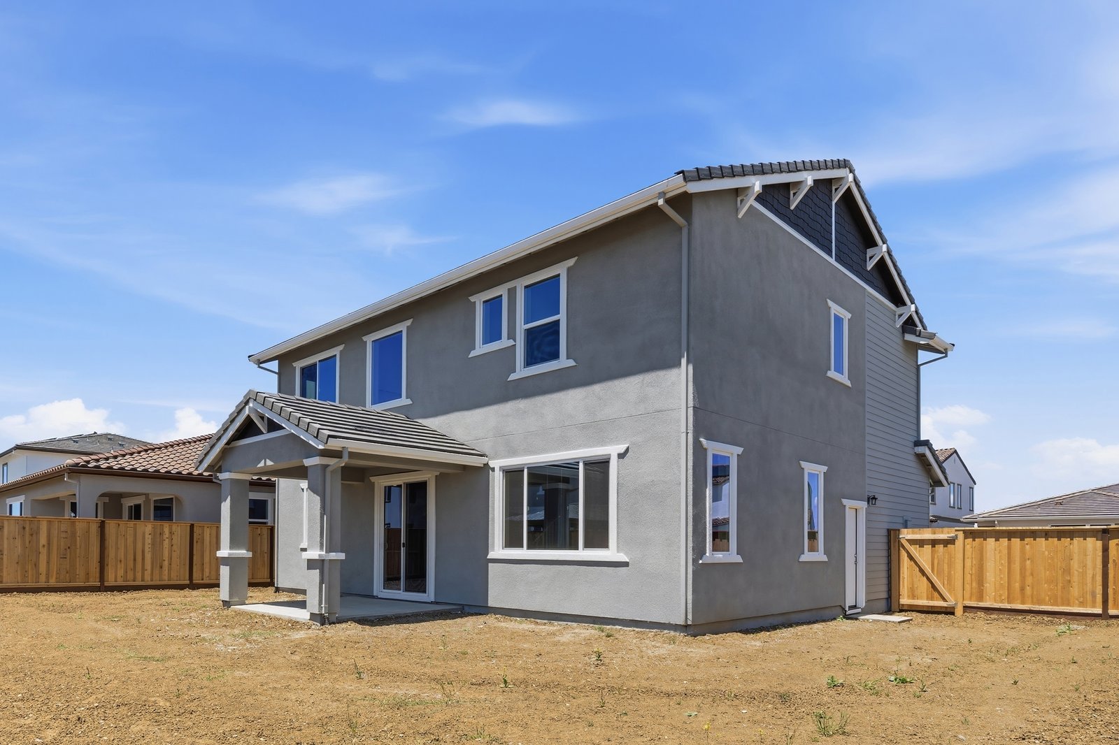 unfinished backyard of two-story gray home with covered patio, and wood fence