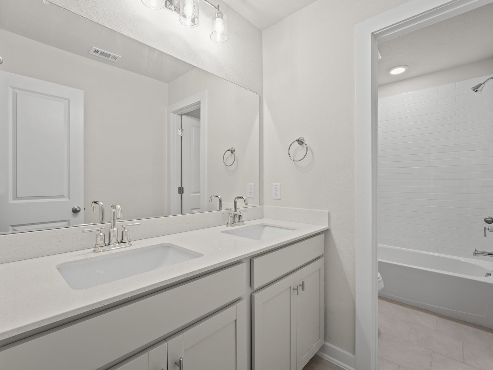 secondary bathroom with dual sinks, soaking tub and white cabinets