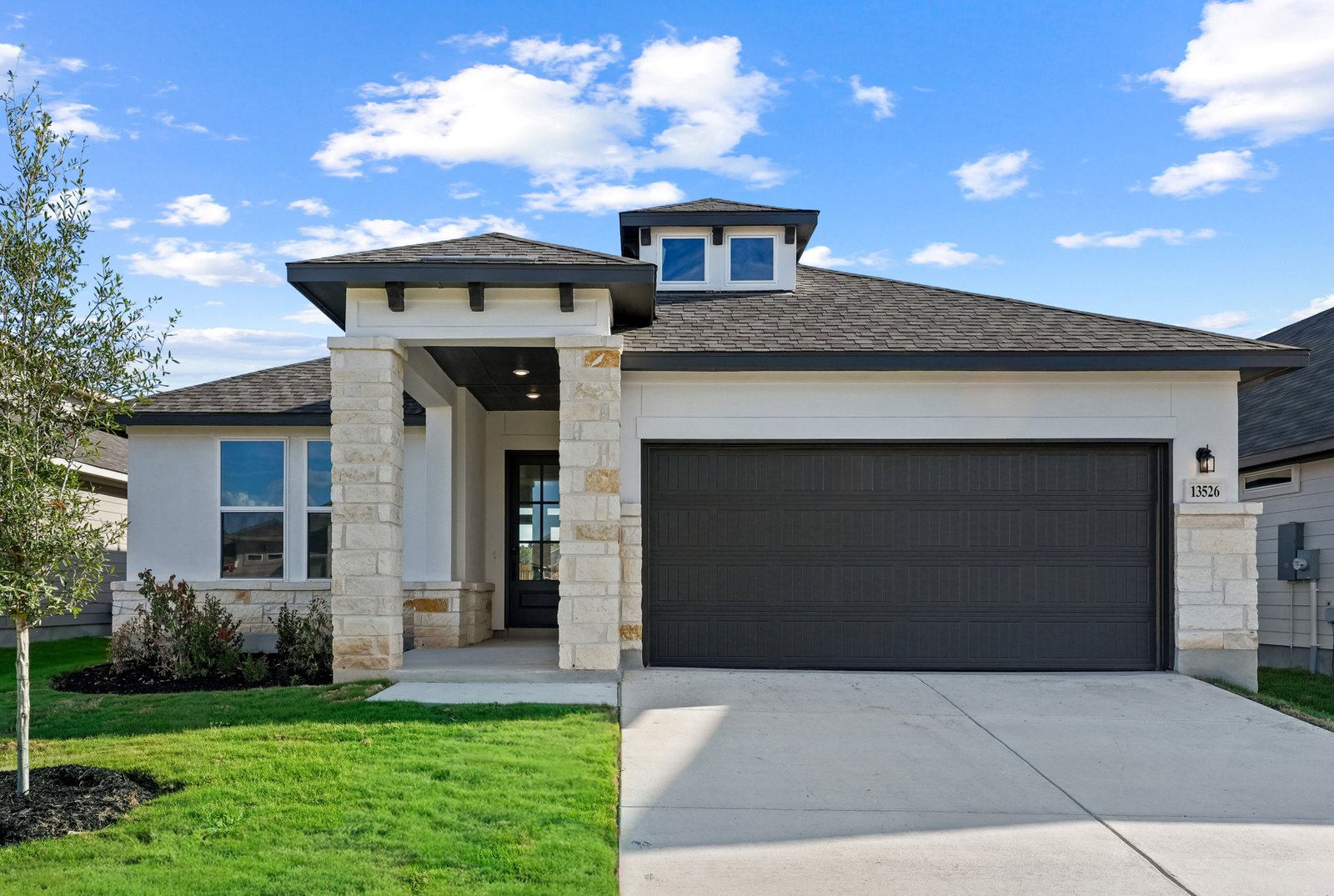 home with brick, windows, a tree and landscaped grass