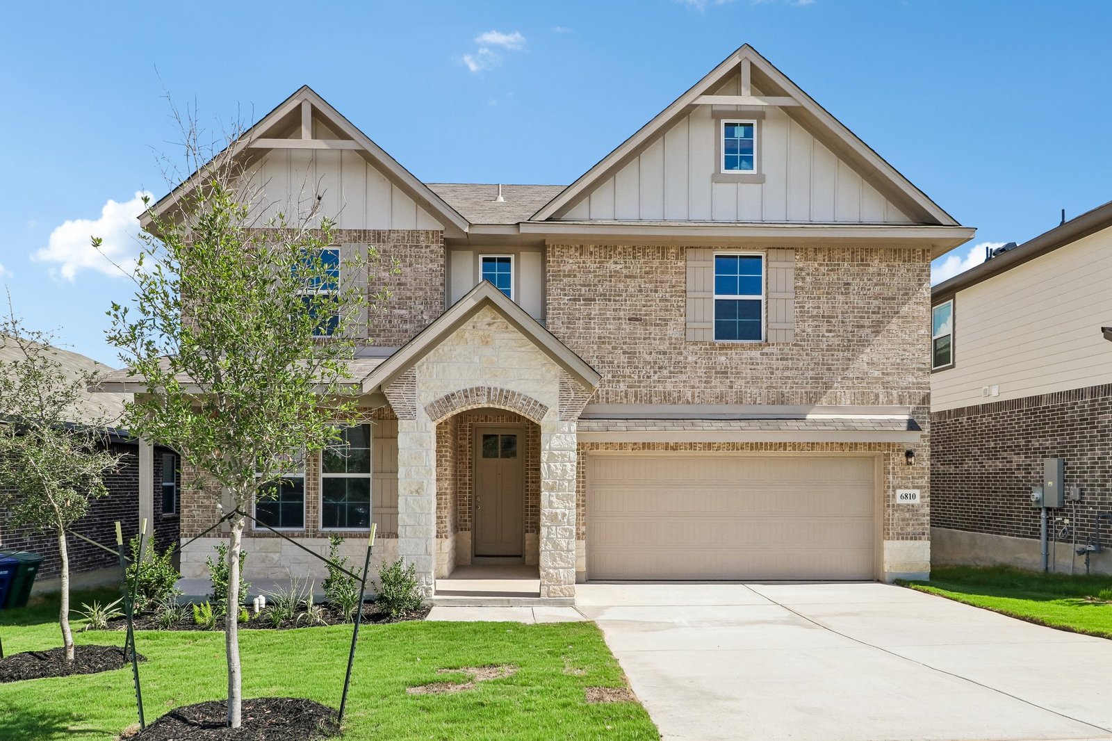 home with brick, windows, a tree and landscaped grass