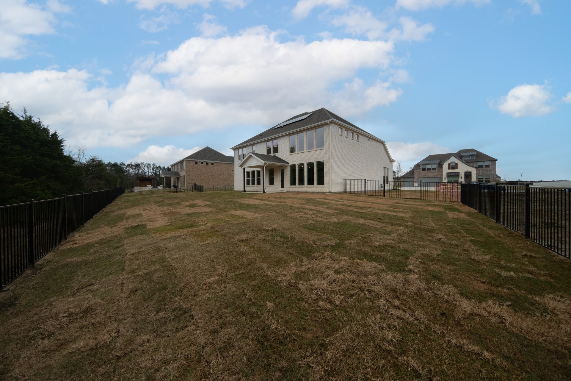 large backyard with wrought iron fence, grass, and covered patio