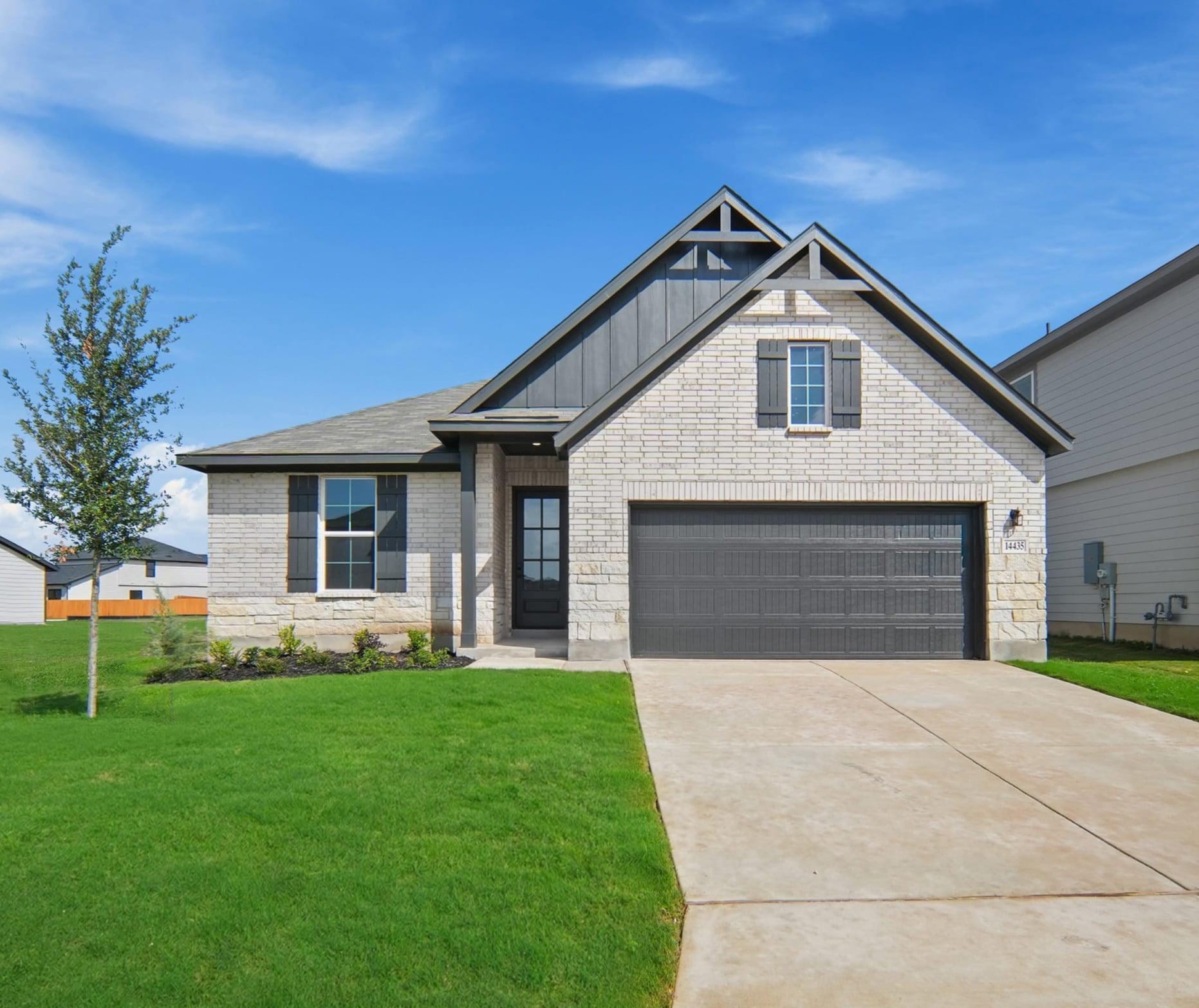 home with brick, windows, landscaped grass and a tree