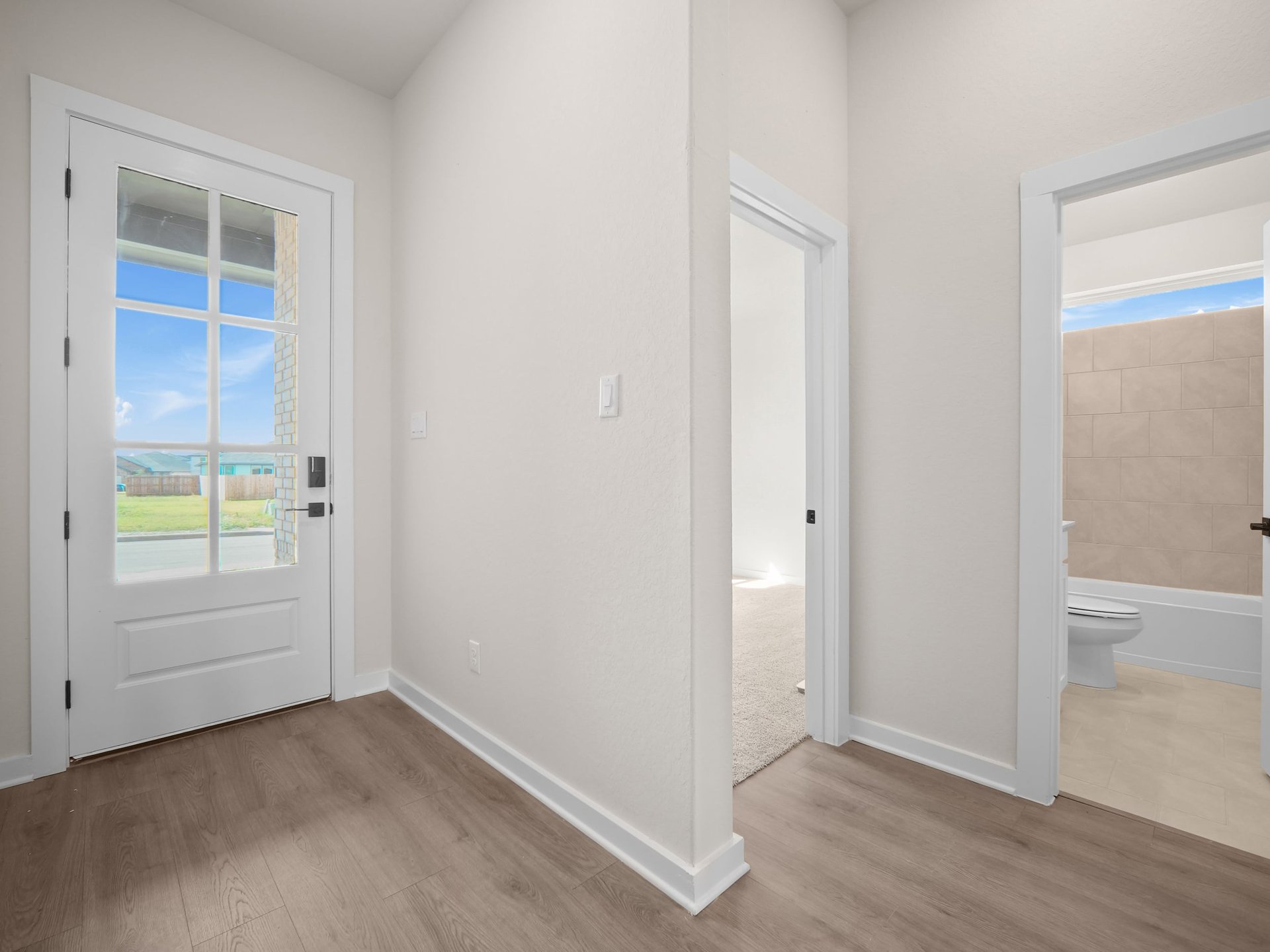 foyer with brown flooring, font door and entrance to secondary bedroom and bathroom