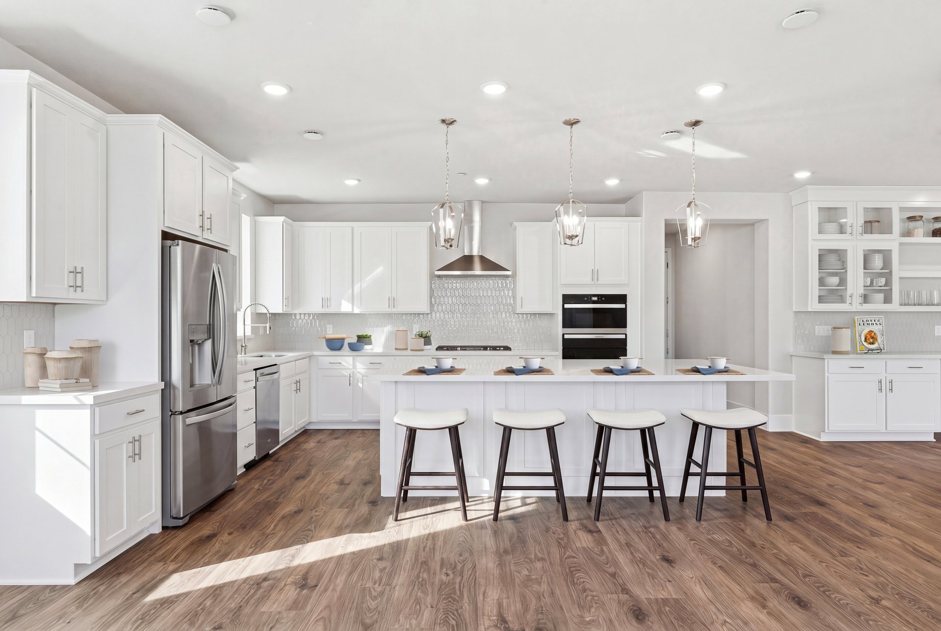 kitchen with white cabinets & counters, wood floors, three brushed nickel pendant lights above island, and four espresso barstools