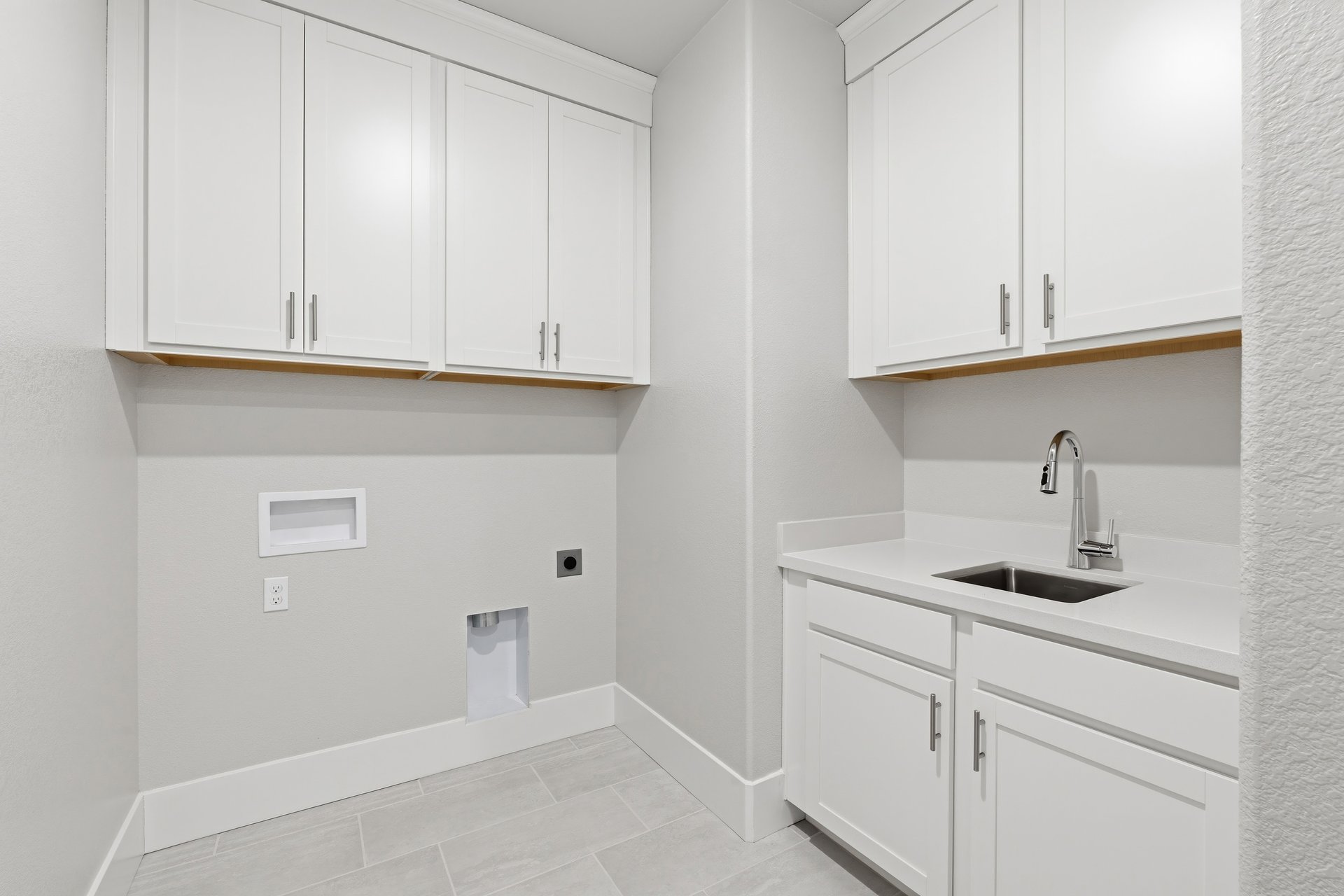laundry room with white upper & lower cabinets, sink, and tan tile floors
