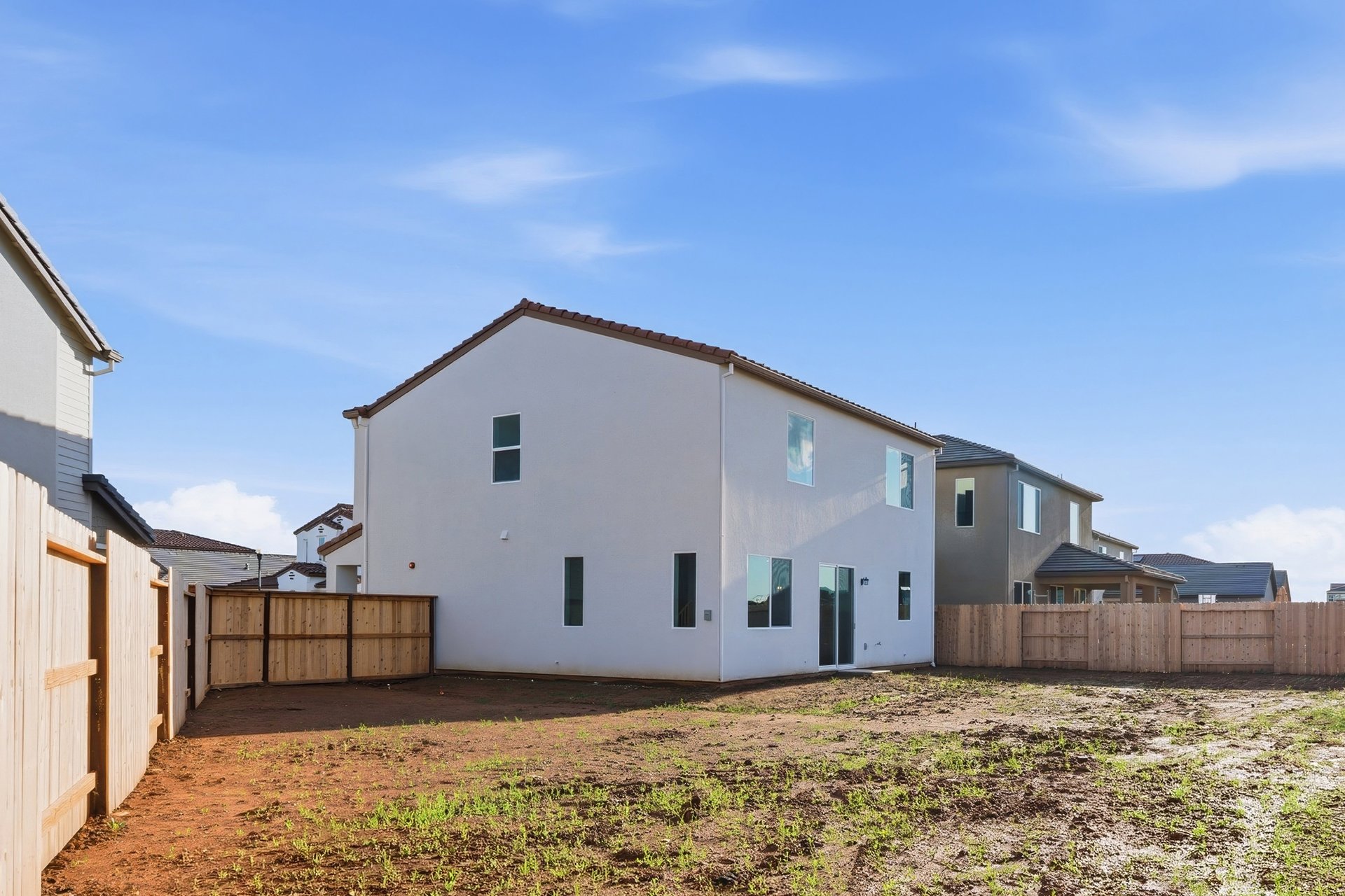 unfinished backyard of two-story white home with wood fence