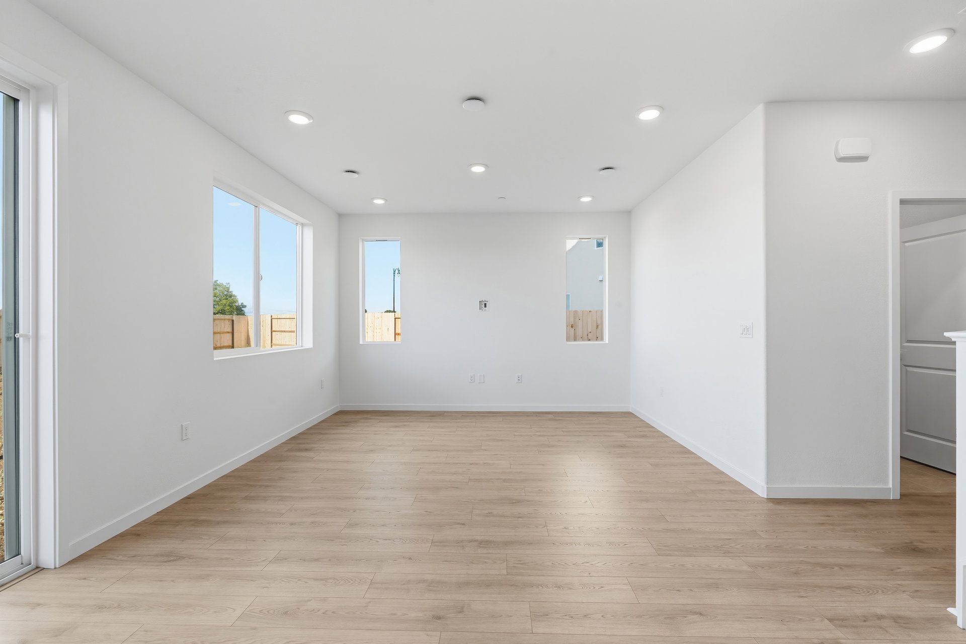 great room with light wood floors, white walls, three windows, and recessed ceiling lights