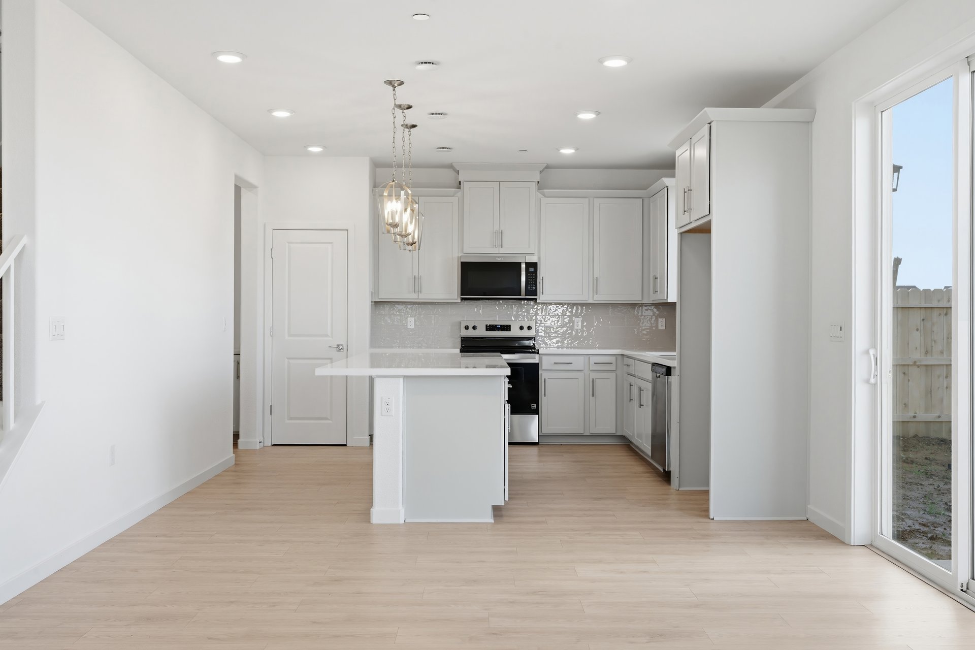 kitchen with light wood floors, white cabinets, island with white counter, and sliding glass door to backyard