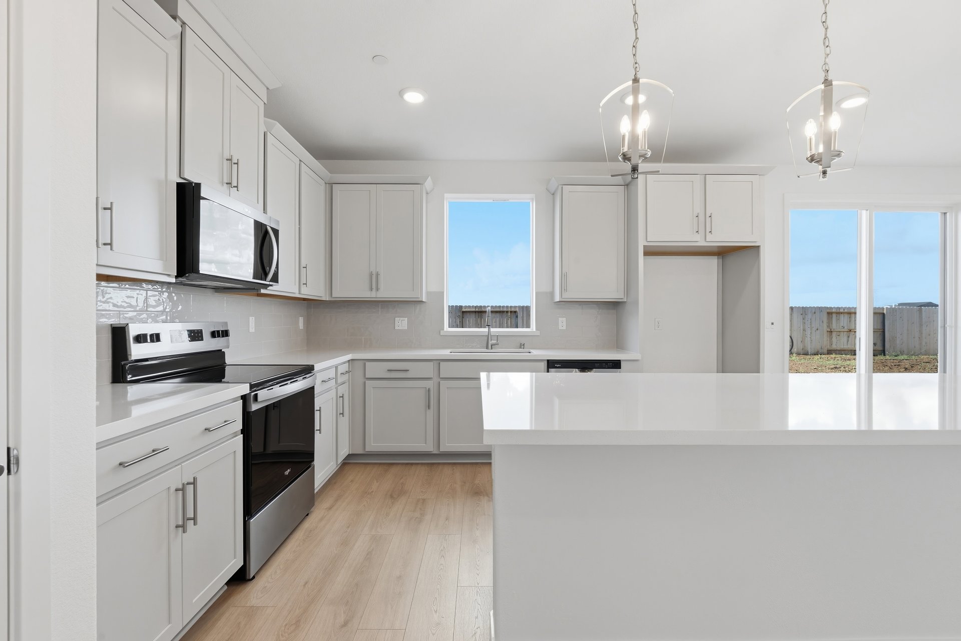 kitchen with white cabinets & counters, light wood floors, window, and two silver light pendants above island