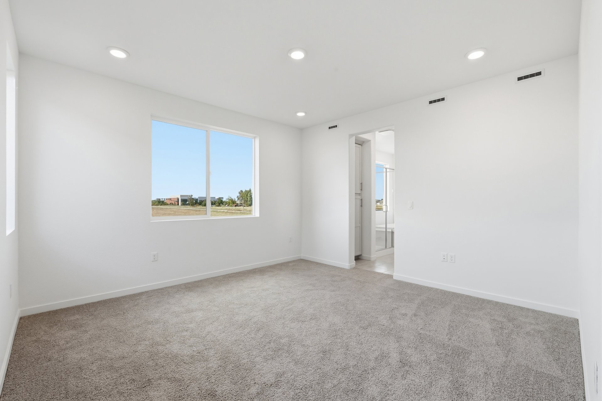 bedroom with tan carpet, white walls, window, and view of attached bathroom