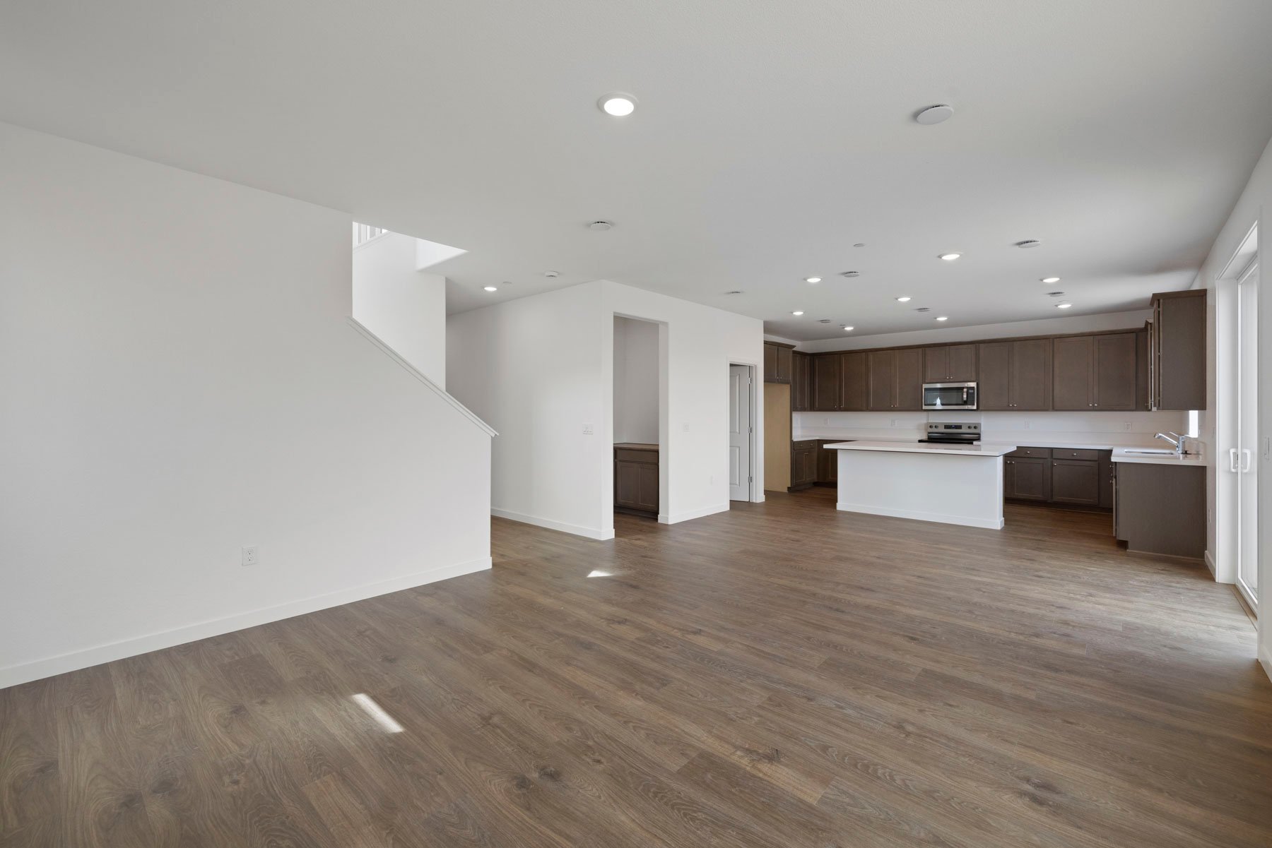 great room with wood floors, white walls, and view of kitchen with brown cabinets