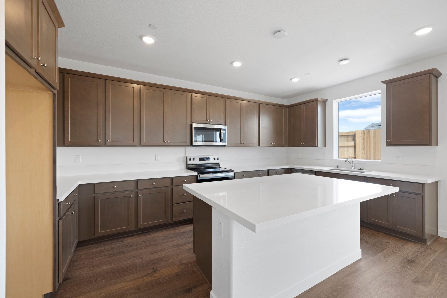 kitchen with brown cabinets, wood floors, white quartz counters, island, and window over sink