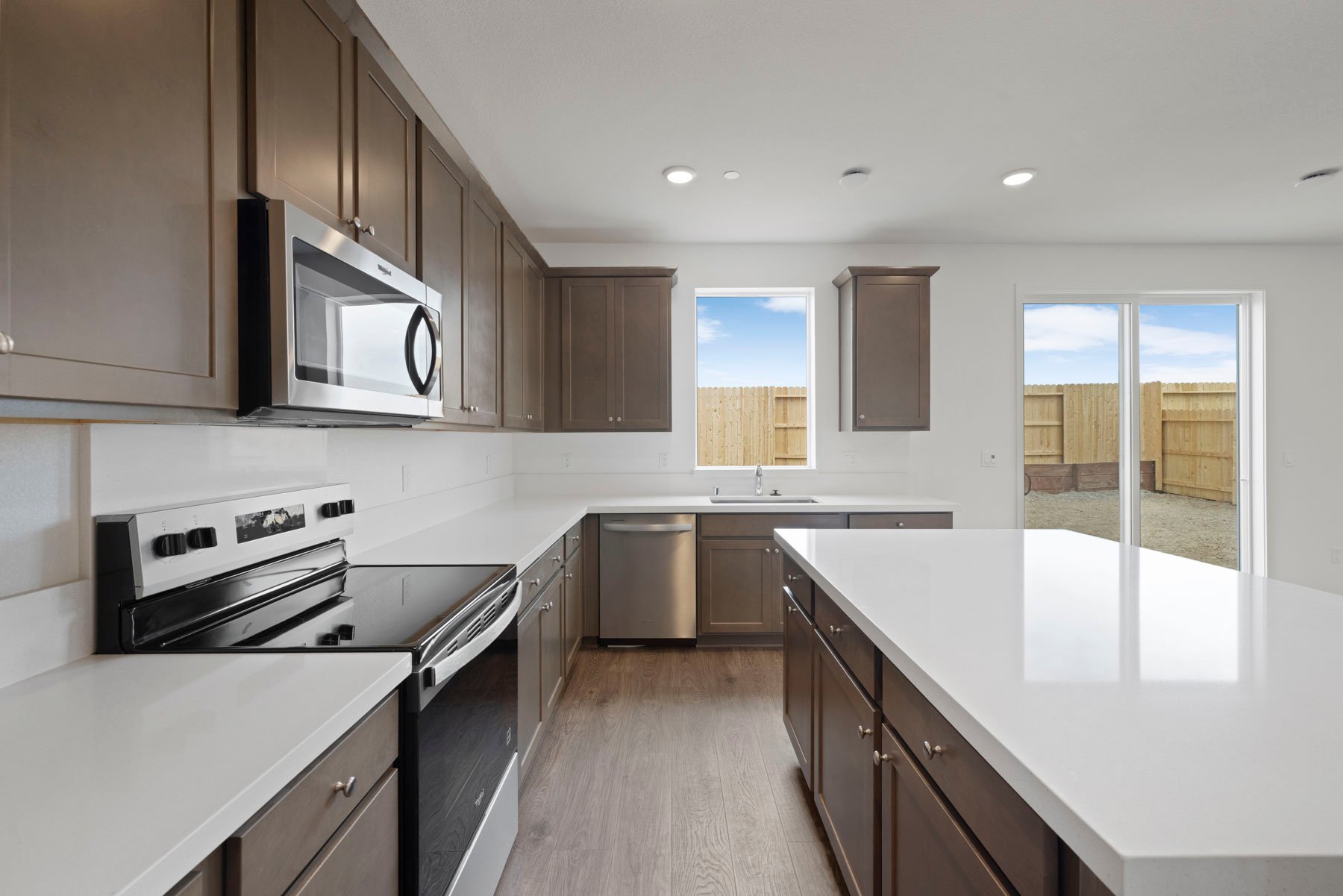 kitchen with brown cabinets, white quartz counters, wood floors, island, and window