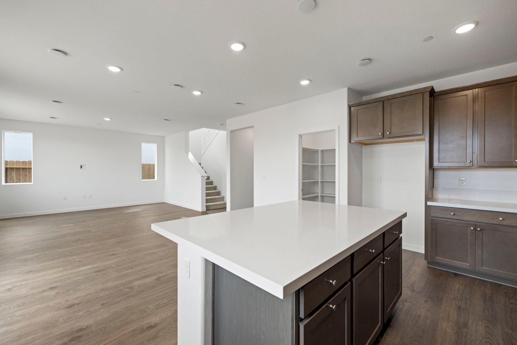 kitchen with brown cabinets, white counters, island, walk-in pantry, and wood floors