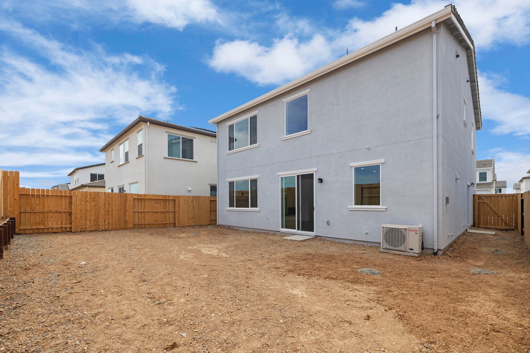 unfinished backyard of two-story gray home with wood fence
