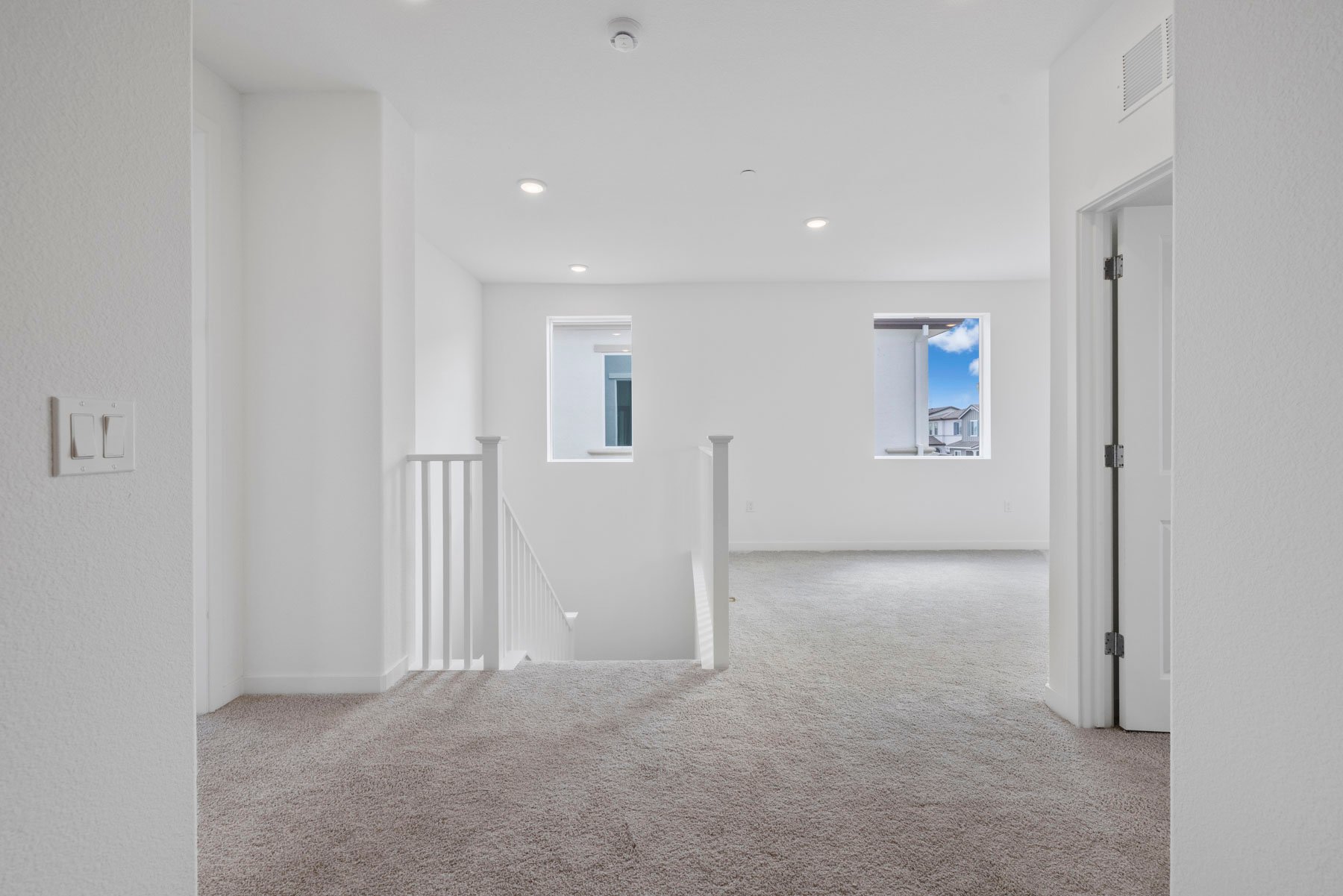 loft with tan carpet, white walls, recessed ceiling lights, and two windows