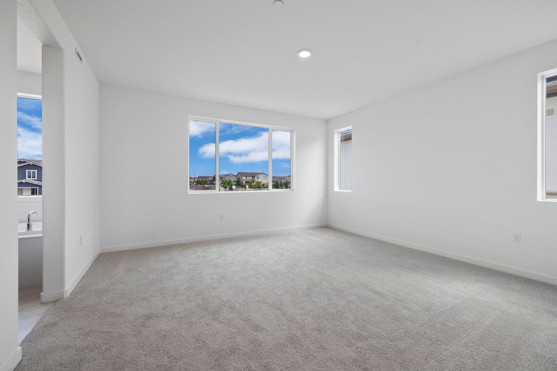 large bedroom with tan carpet, white walls, and three windows