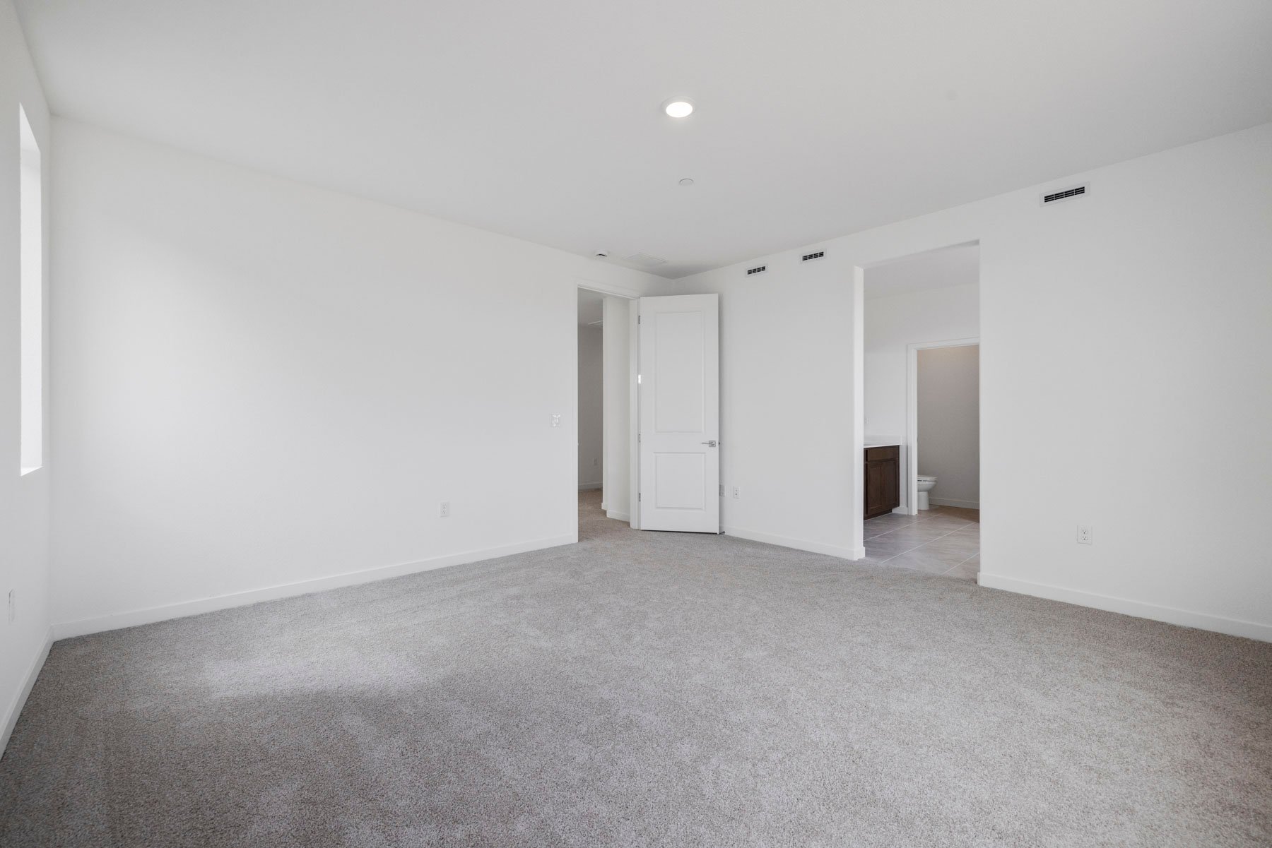 bedroom with tan carpet, white walls, and view of attached bathroom
