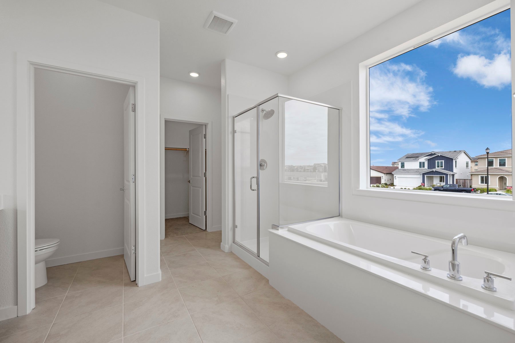 bathroom with tan tile floors, walk-in shower, and large window above tub