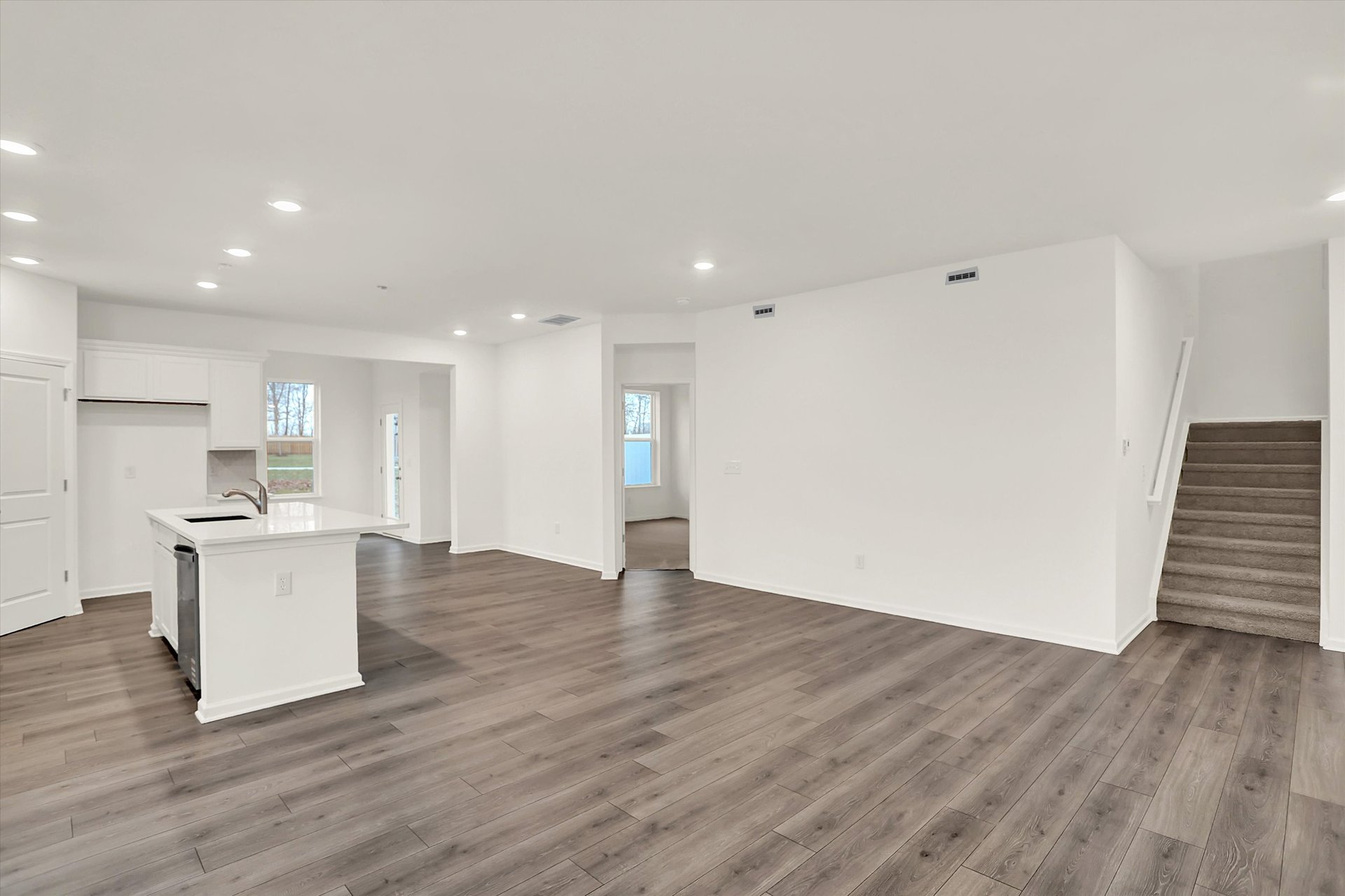 open-concept great room and kitchen with wood plank flooring with white walls