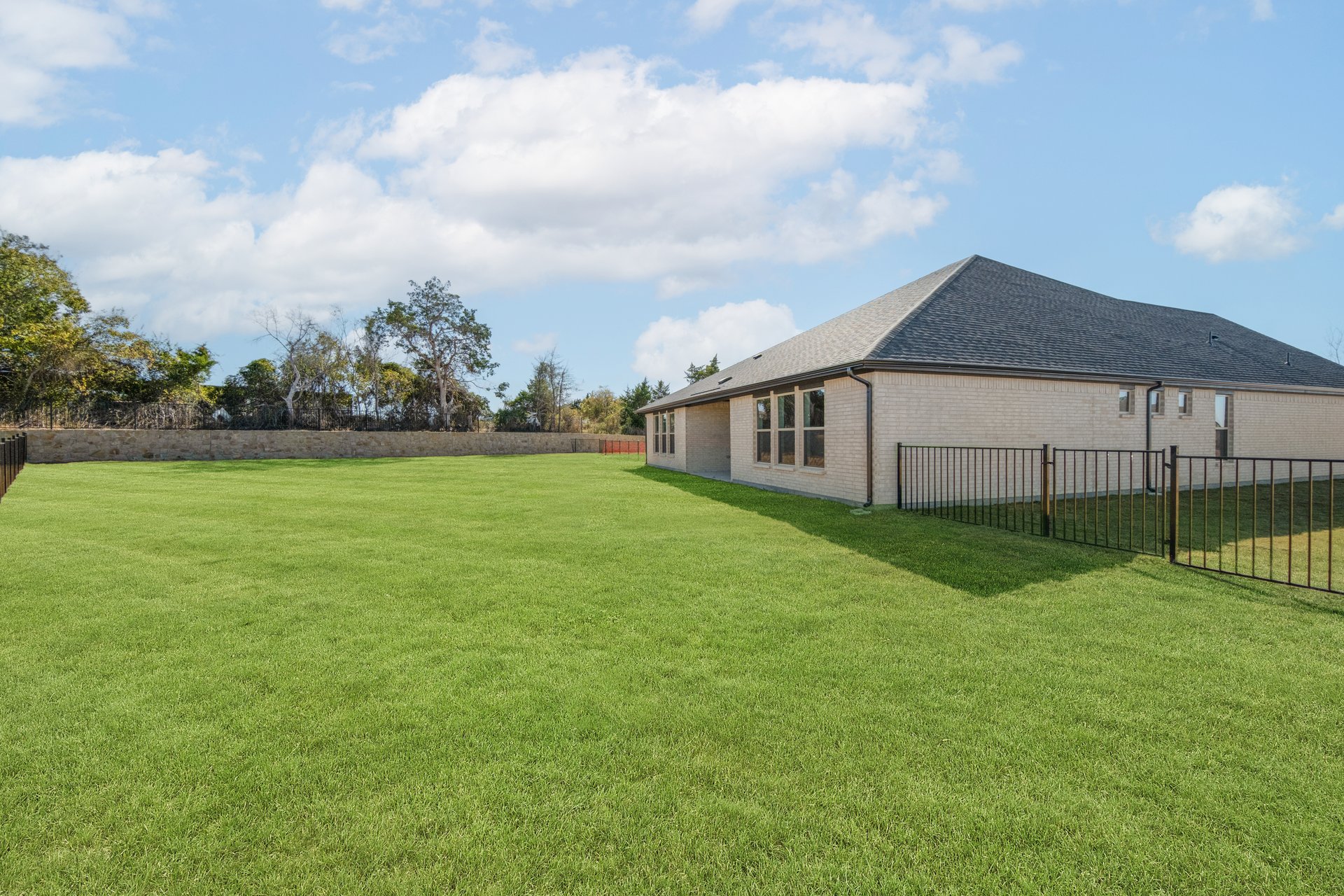 large backyard with wrought iron fence, grass, and covered patio