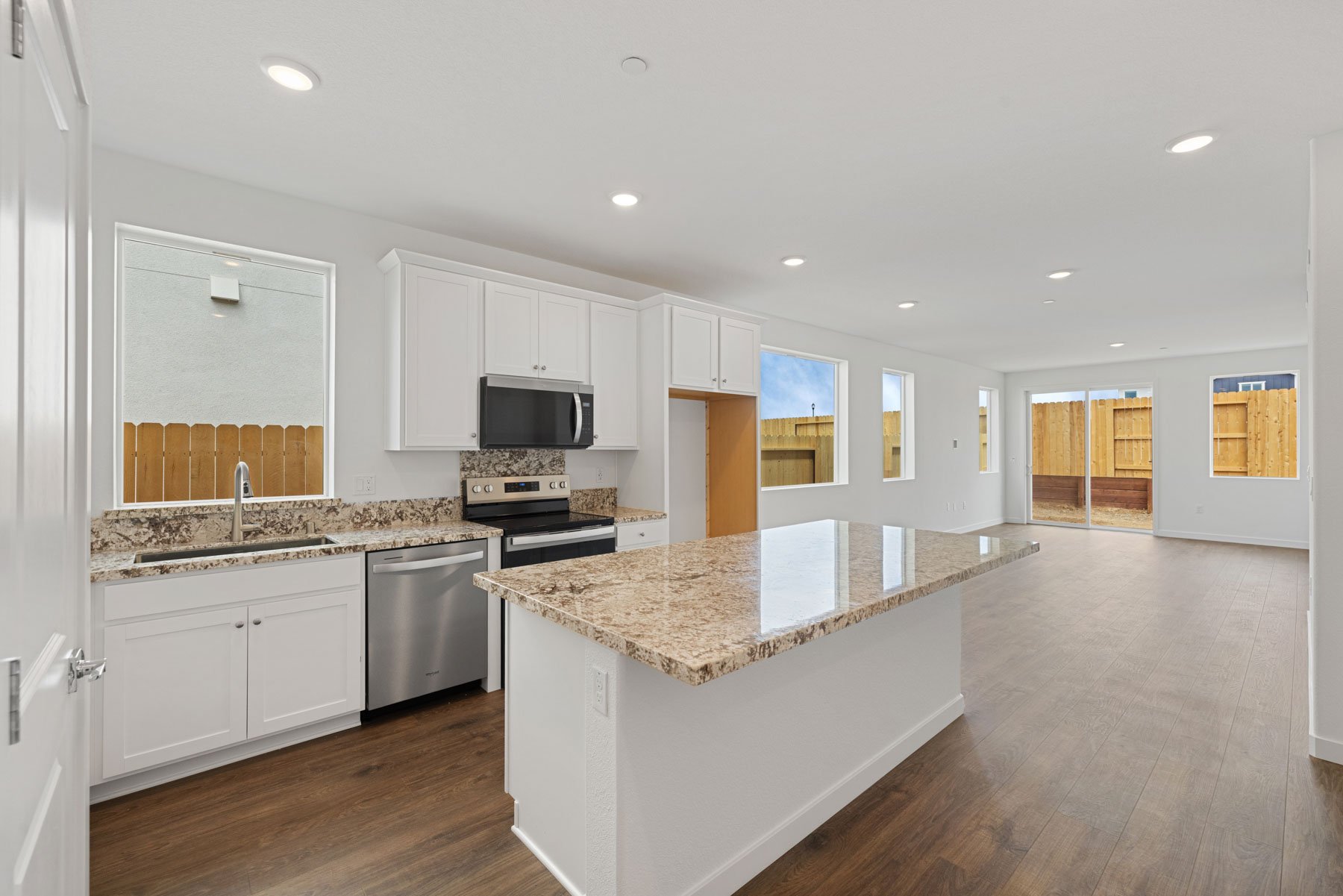kitchen with white cabinets, granite counters, island, wood floors, and window above sink