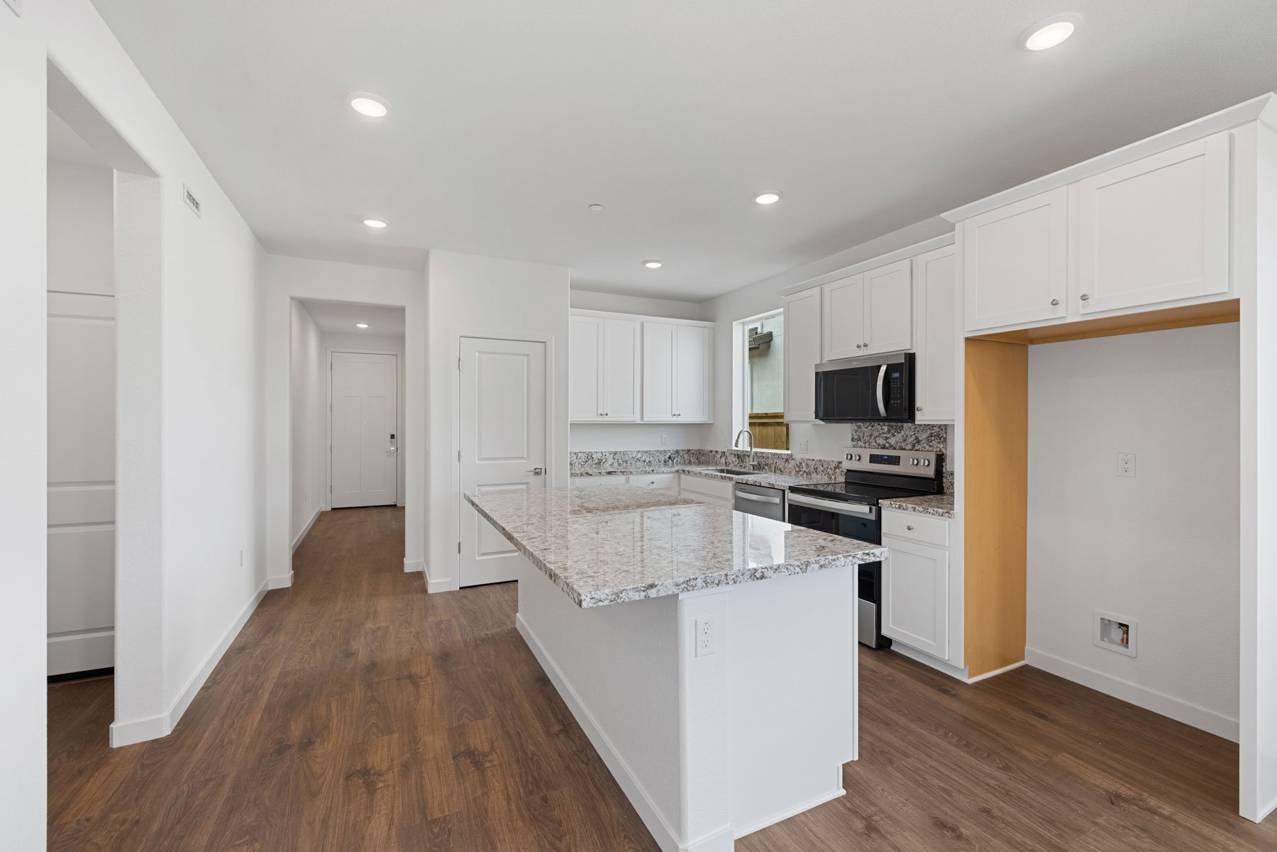 kitchen with wood floors, white cabinets, granite counters, and view of entry foyer