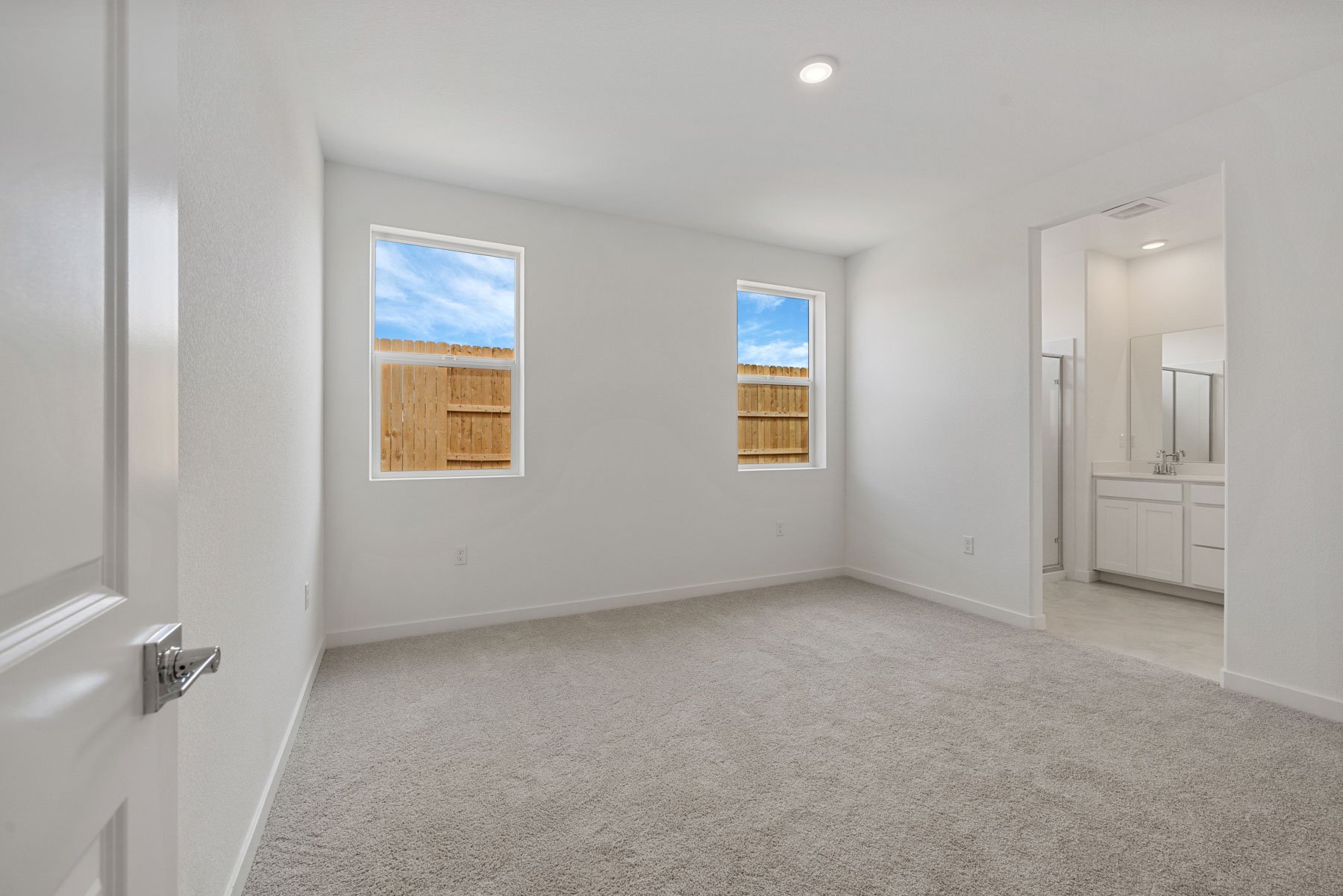 bedroom with light tan carpet, two windows, and view of attached bathroom
