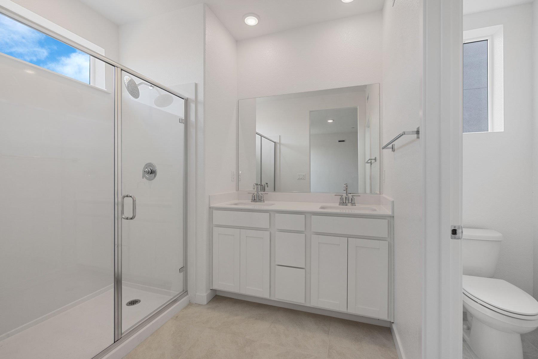 bathroom with white cabinets & counters, two sinks, and window above large walk-in shower with glass enclosure