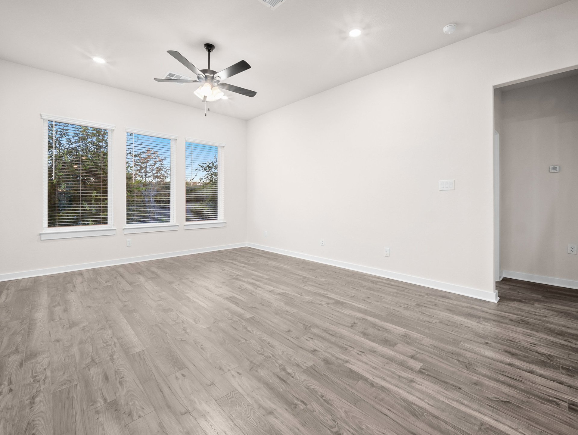 great room with brown flooring, windows & a ceiling fan