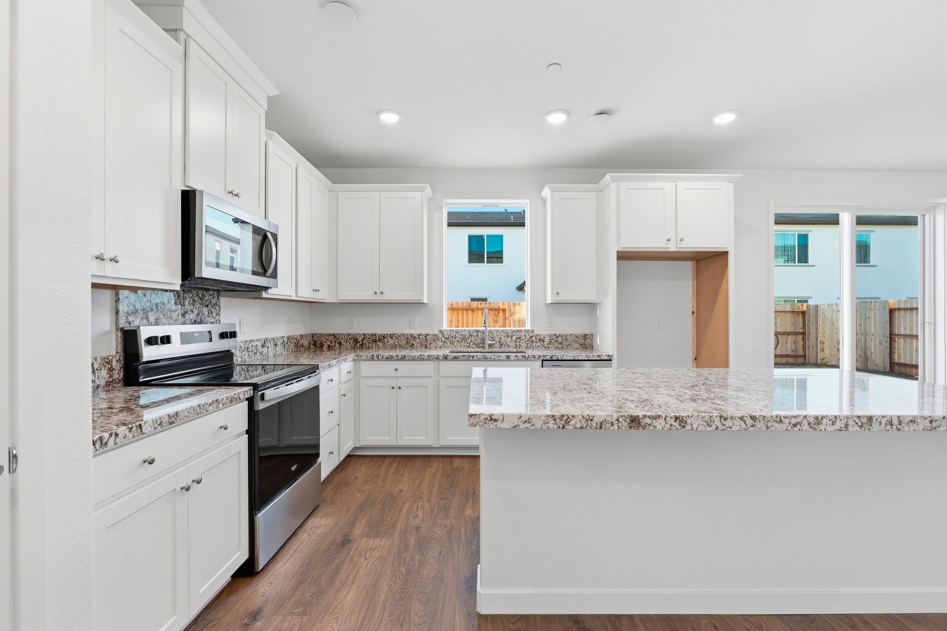 kitchen with white cabinets, granite counters, island, stainless steel appliances, window, and wood floors