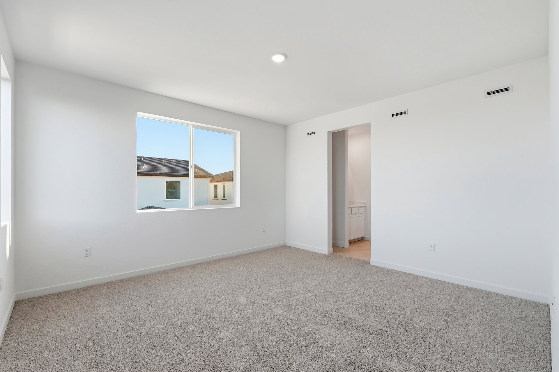 bedroom with tan carpet, white walls, window, and view of attached bathroom