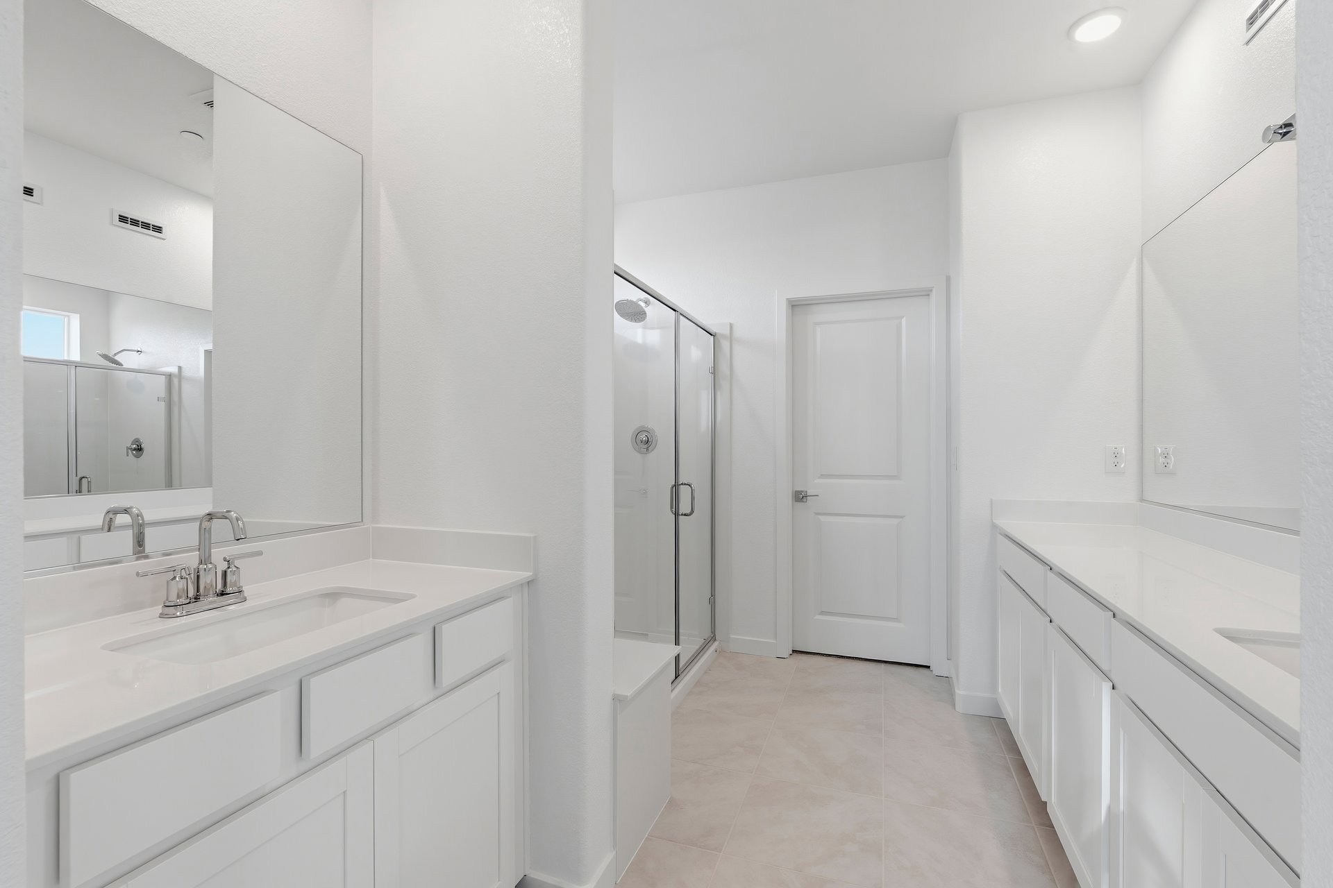 bathroom with white cabinets & counters, tan tile floors, separate vanities, and walk-in shower