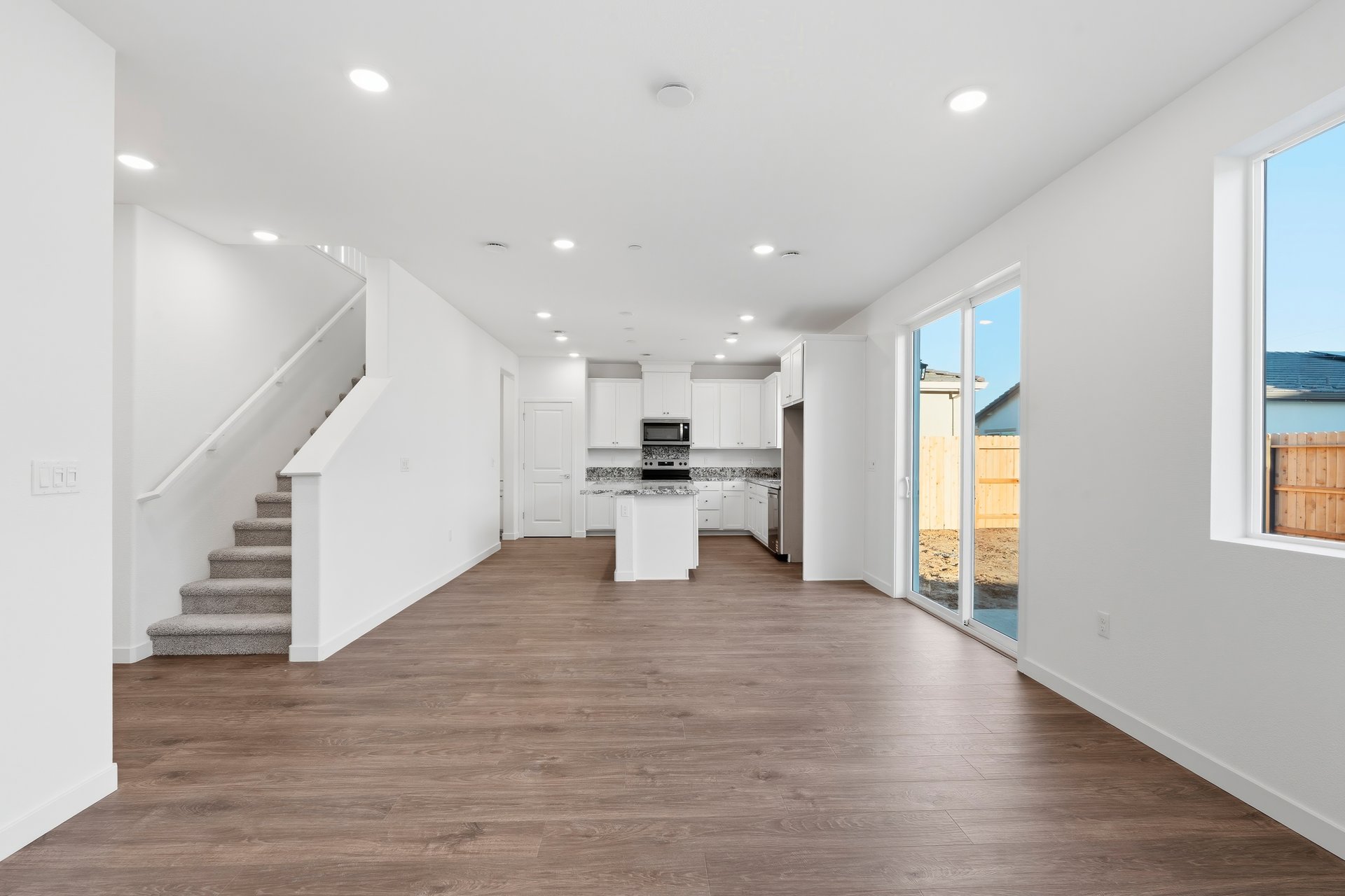 great room with wood floors, white walls, sliding glass door to backyard, and view of kitchen