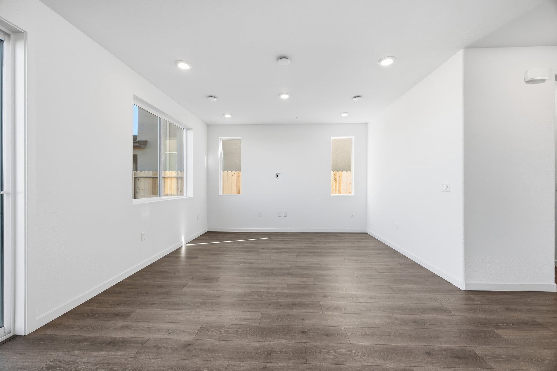 great room with wood floors, white walls, and three windows