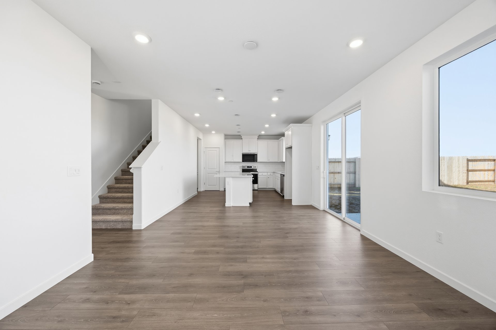 great room with wood floors, white walls, recessed ceiling lights, window, and sliding glass door