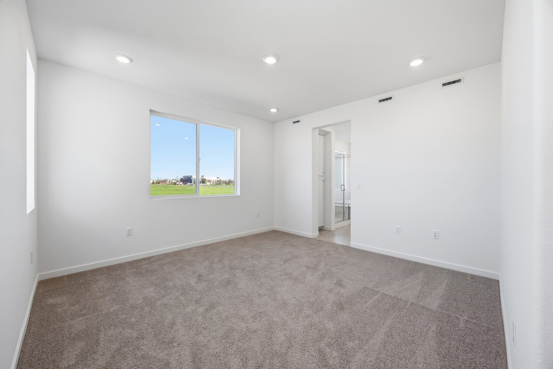 bedroom with tan carpet, white walls, window, and view of attached bathroom