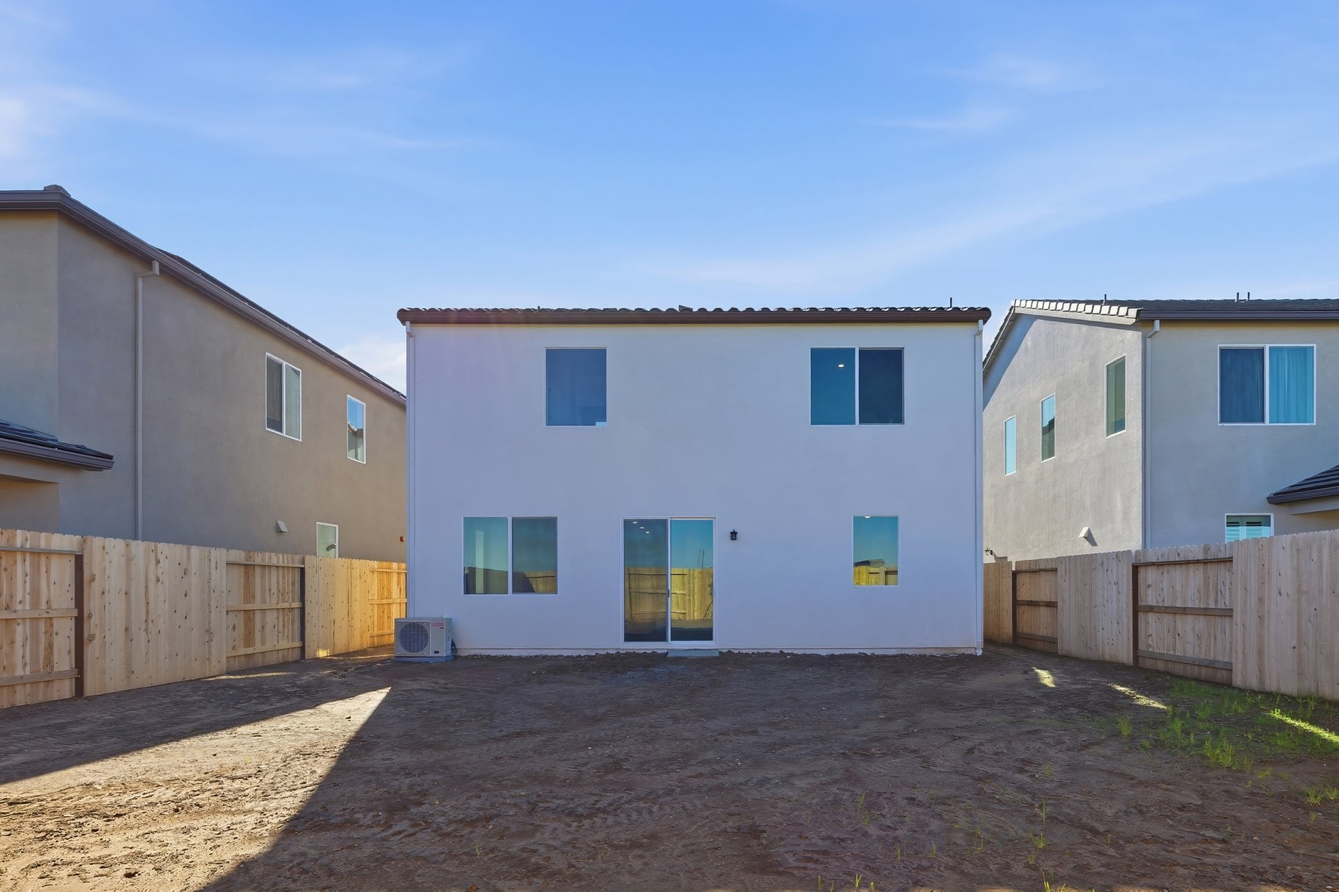 unfinished backyard with wood fence, and back exterior view of two-story white home