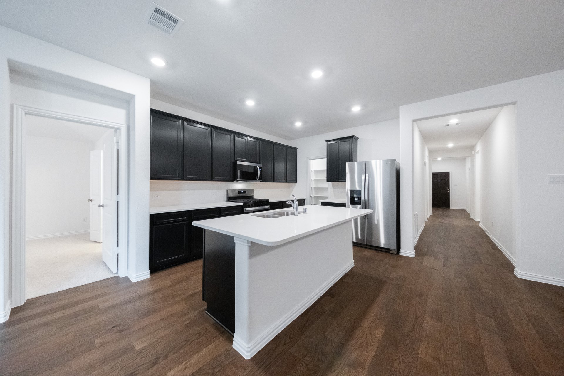 open kitchen with black cabinets and hardwood flooring