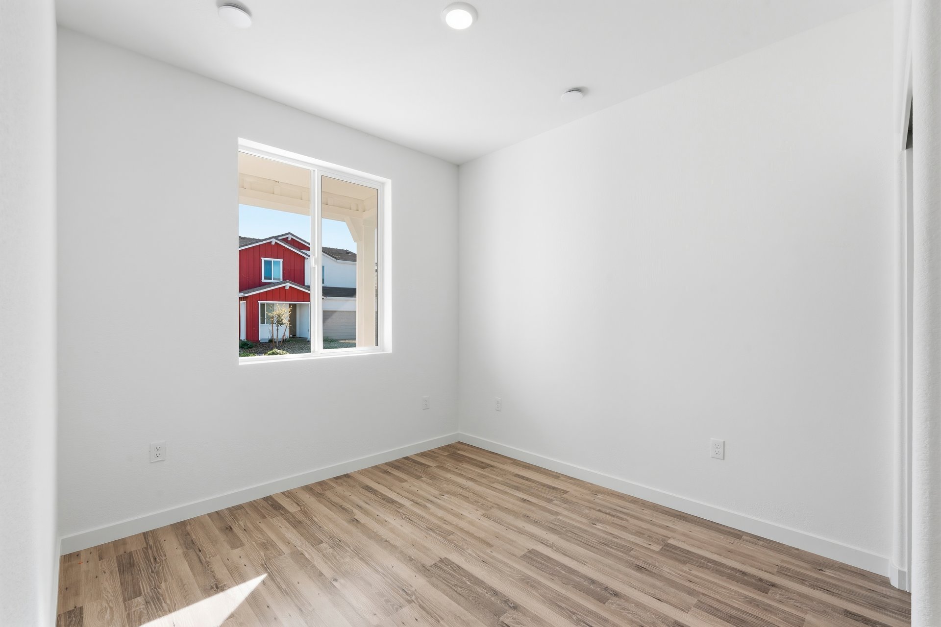 bedroom with wood floors, white walls, and window looking out to the front covered porch