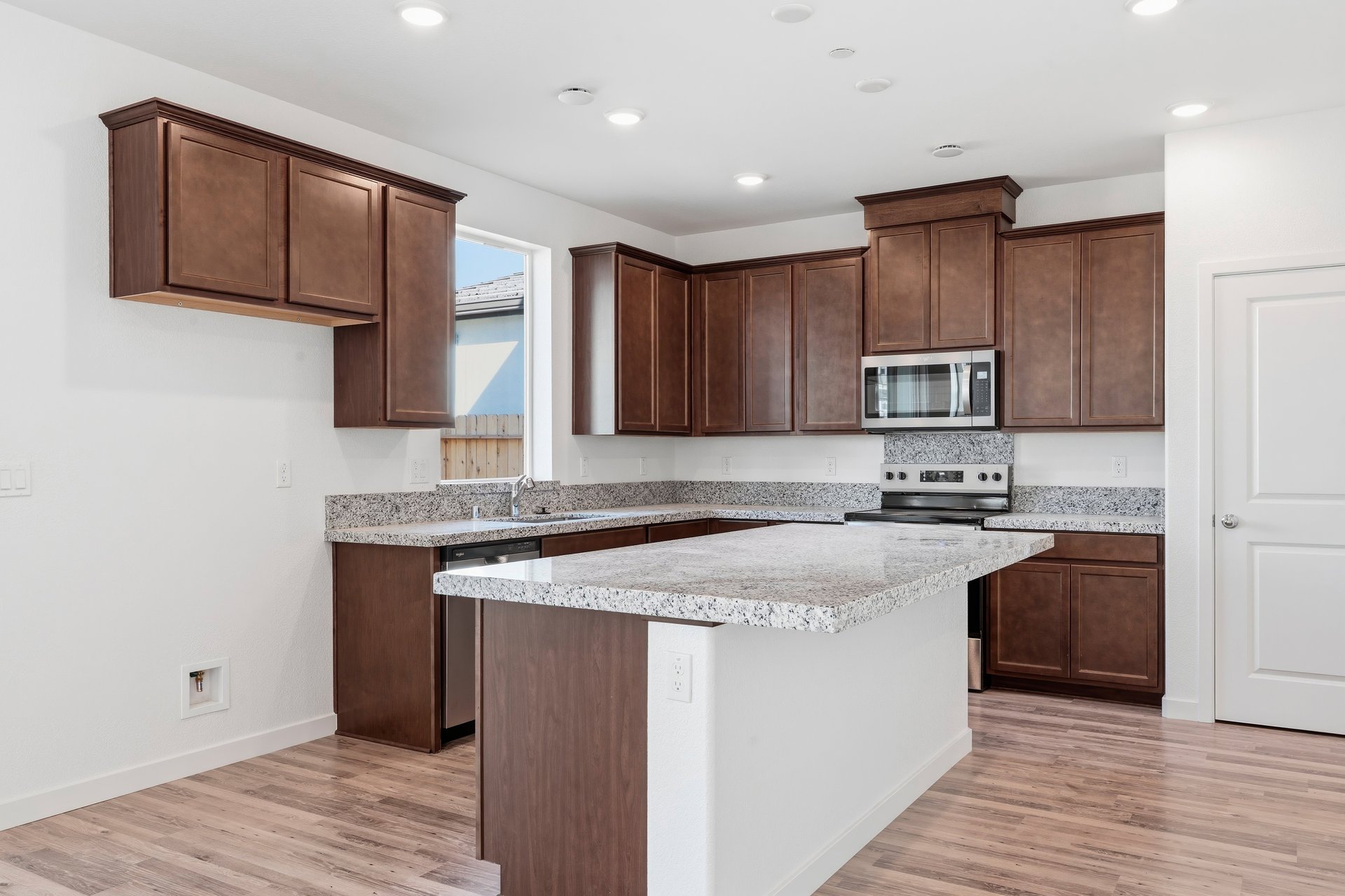 kitchen with brown wood cabinets, island with granite counters, window, and stainless steel appliances