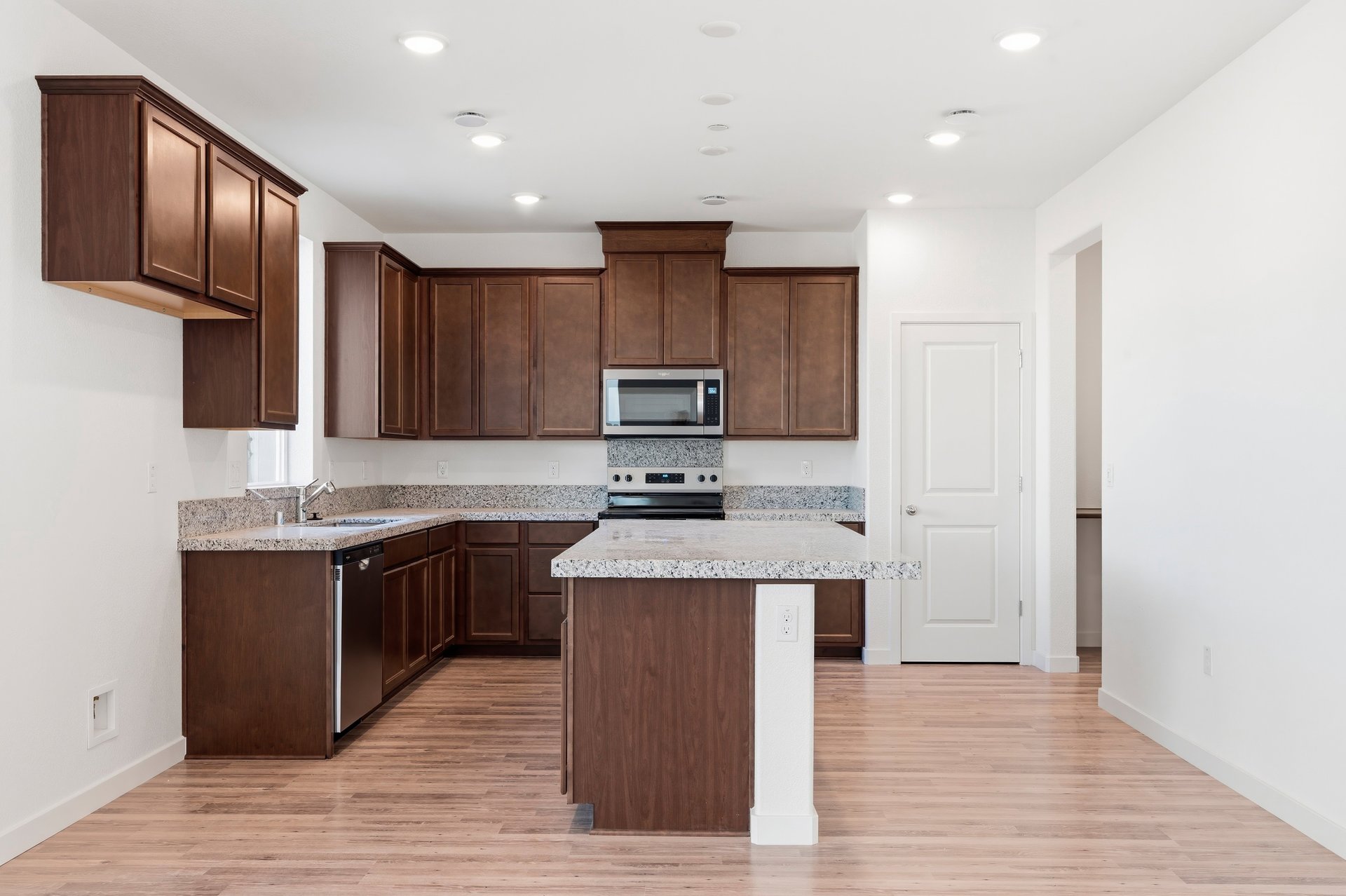 kitchen with wood floors, brown wood cabinets, island, granite counters, and recessed ceiling lights