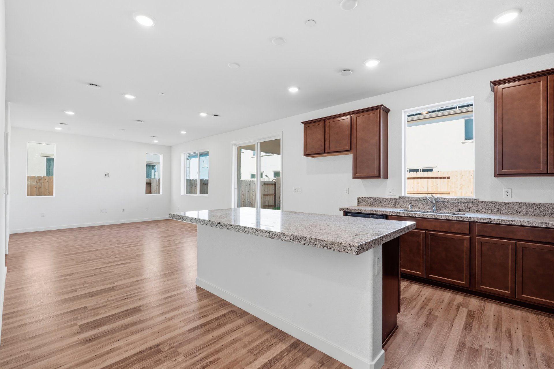 kitchen with brown wood cabinets, granite counters, wood floors, island, and window above sink